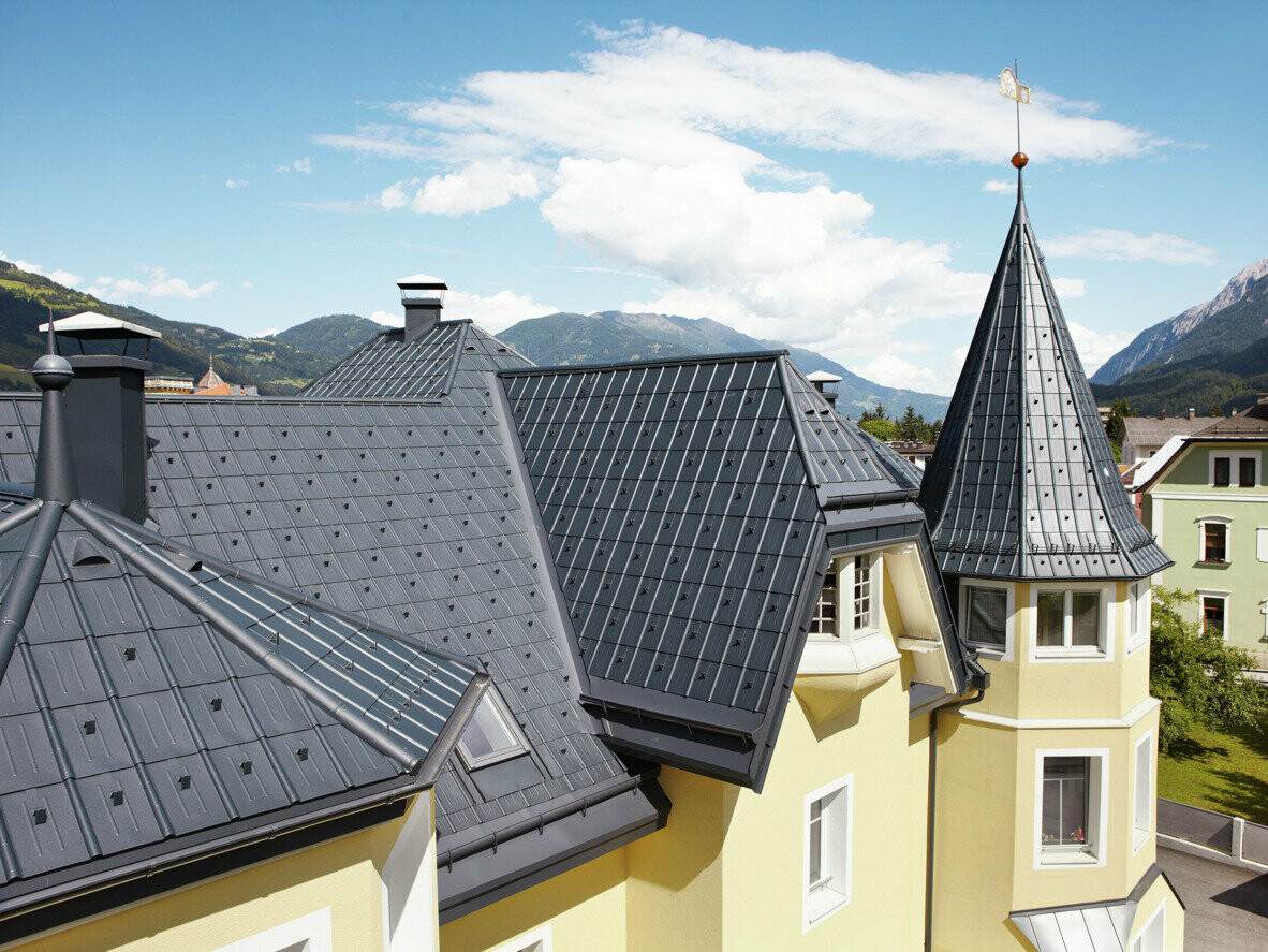 Gebouw met veel details, torens en hoekige dakoppervlakken; het dak is bekleed met de PREFA dakpan in antraciet. Het dakafvoersysteem bestaat uit de PREFA hanggoot en de PREFA Ardense goot in antraciet.