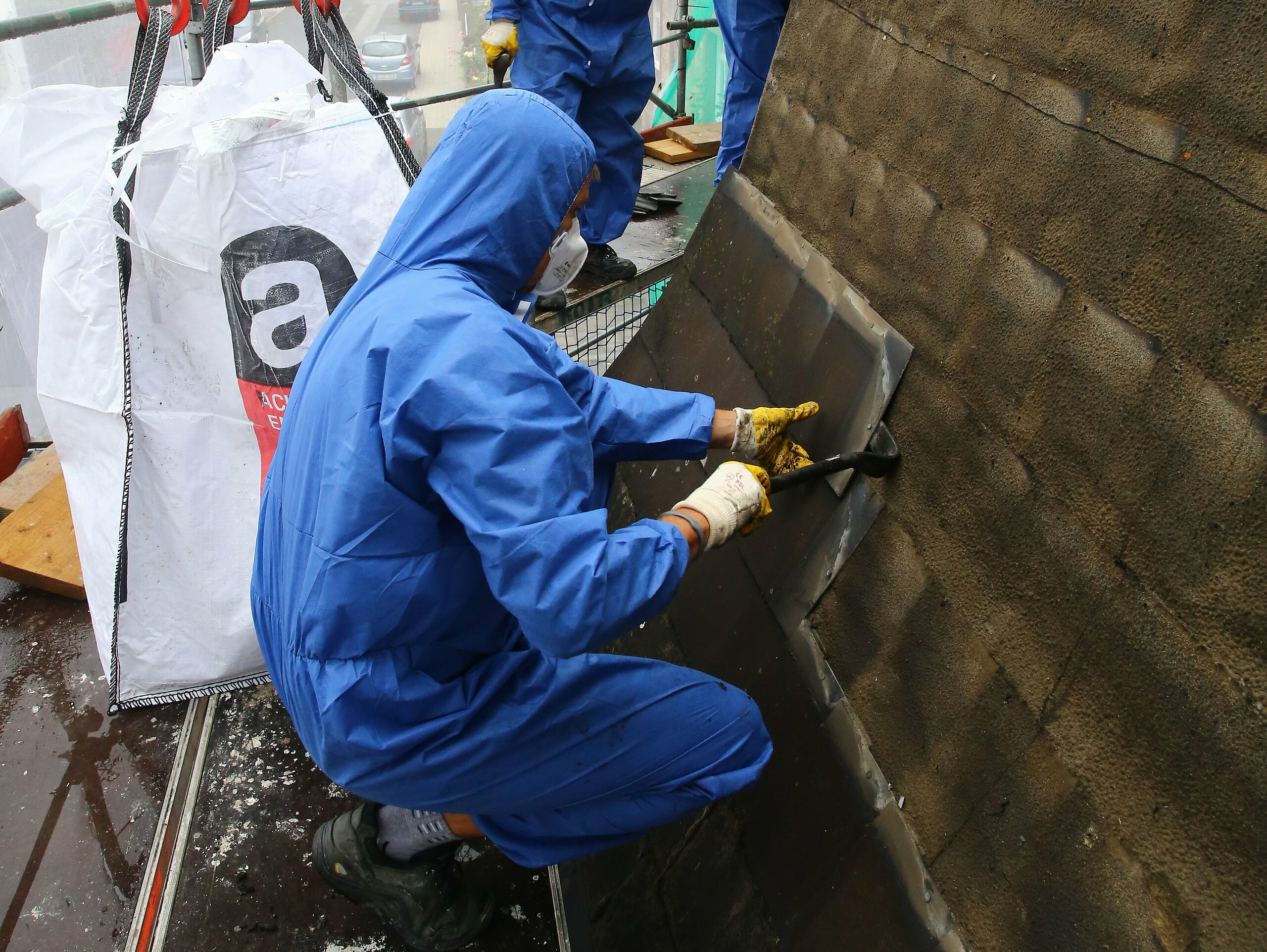 Geschoolde werkman met mondbescherming bij het demonteren en verwijderen van de asbesthoudende, oude dakbedekking