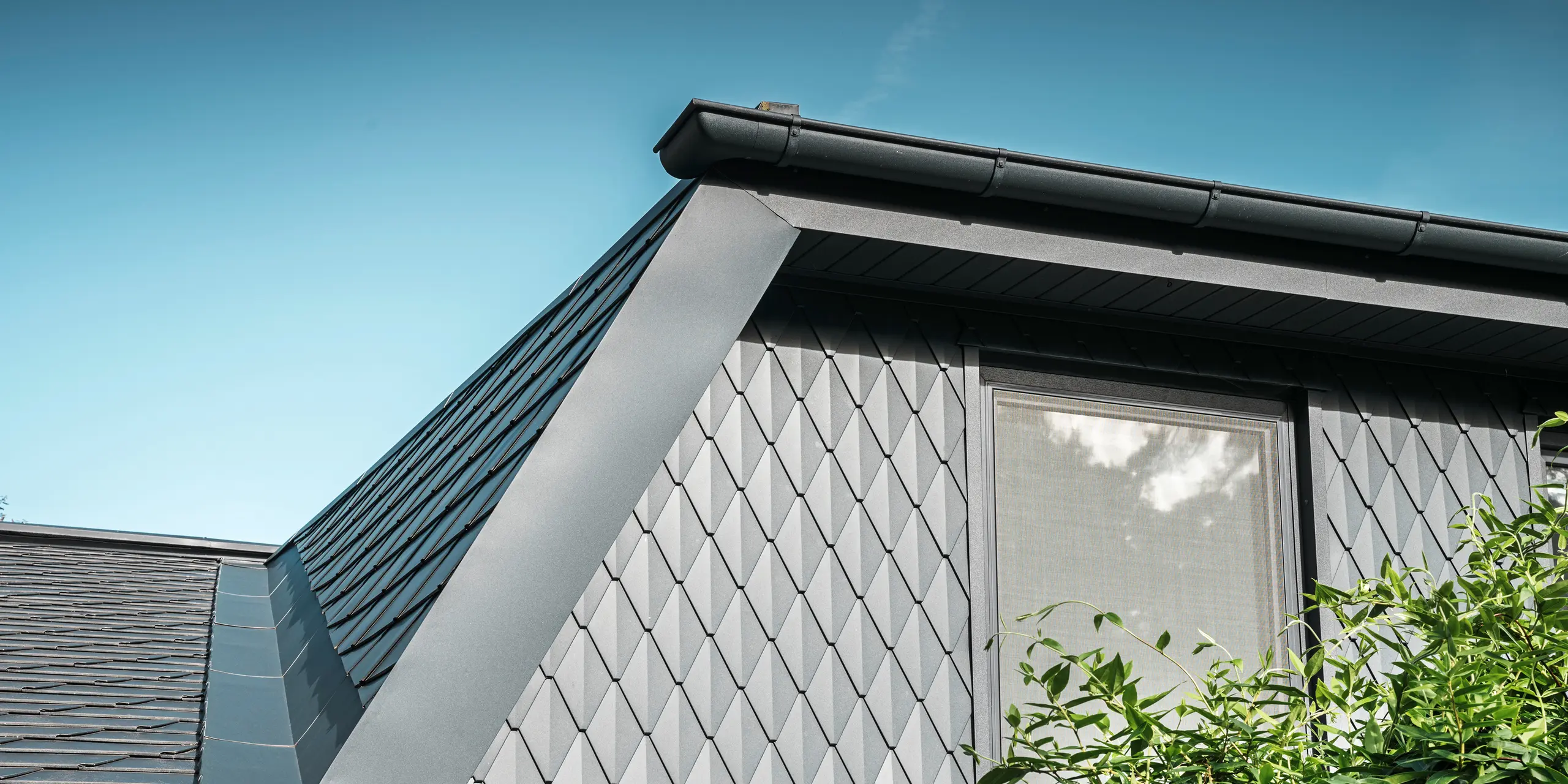 Trapeziumvormige dakkapel van een eengezinswoning in Mechernich, bekleed met kleine PREFA daklosange in P.10 antraciet. Het dak is bedekt met PREFA dakschindels DS.19 in dezelfde kleur. De hoogwaardige aluminium bekleding zorgt voor weerbestendigheid en een moderne, esthetische uitstraling.