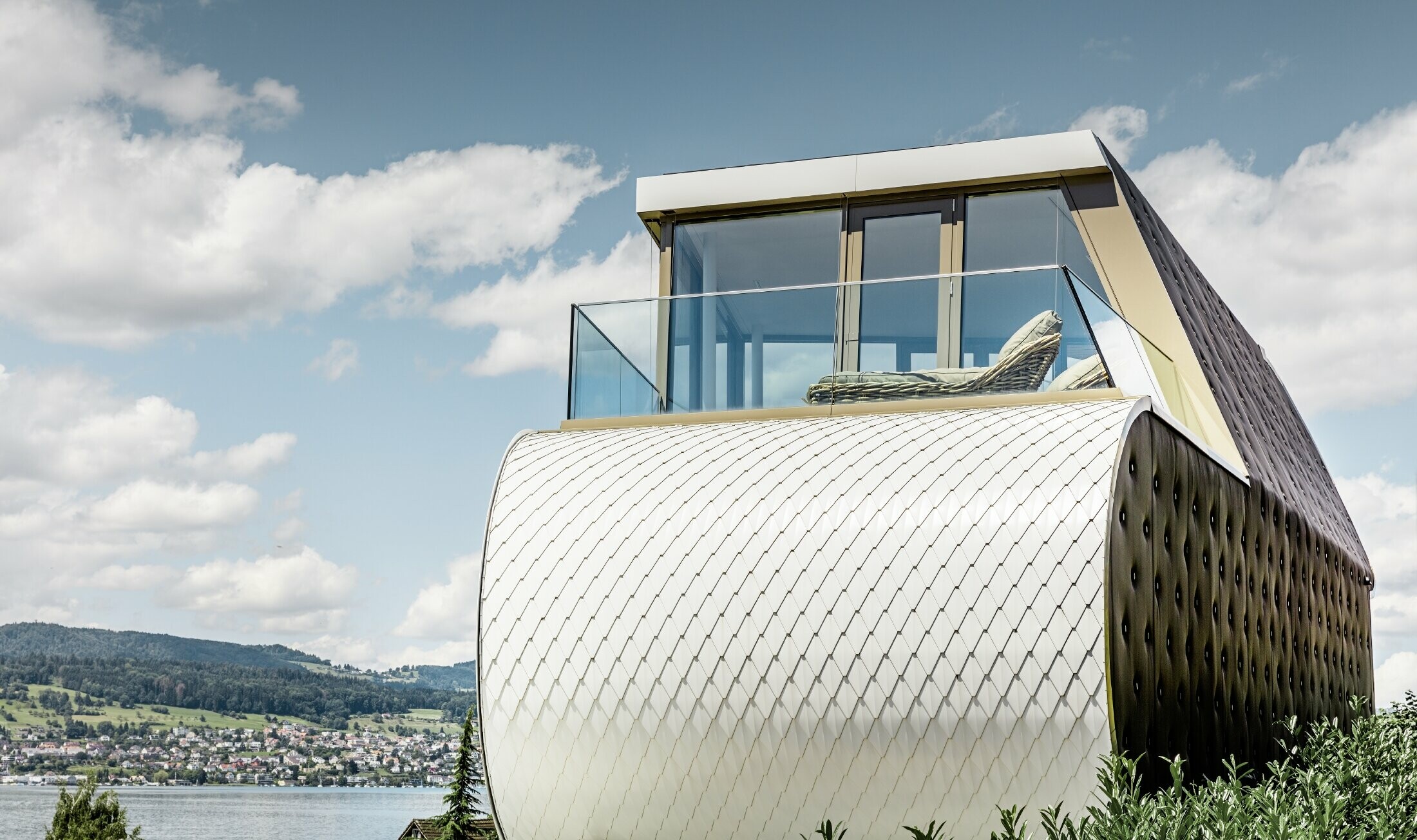 Zijaanzicht van het prachtige Flexhouse, ontworpen door architect Carmenzin; de foto toont een van de gebogen buitenmuren die bekleed is met de geschubde aluminiumgevel van PREFA in zuiver wit.