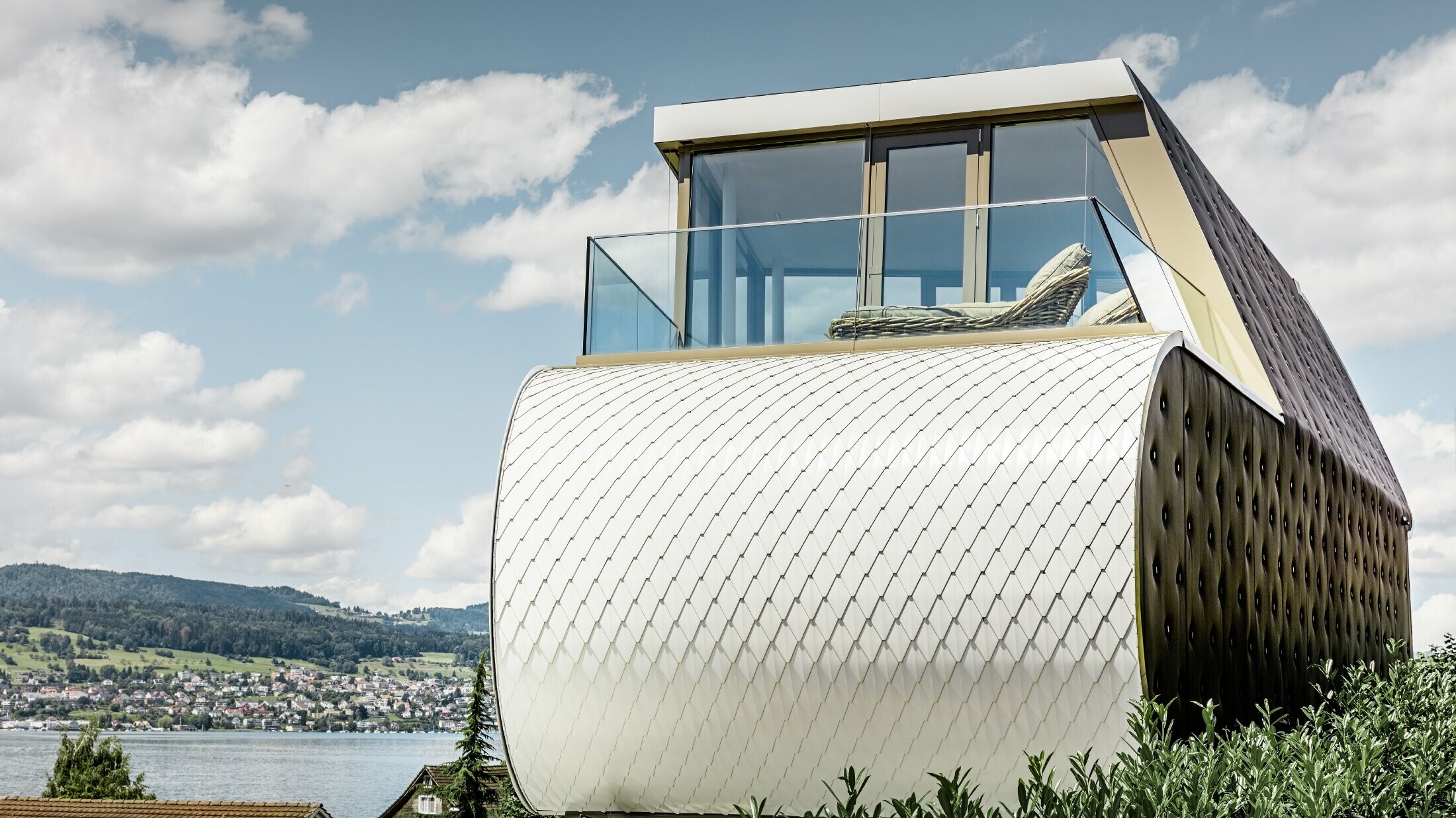 Zijaanzicht van het prachtige Flexhouse, ontworpen door architect Carmenzin; de foto toont een van de gebogen buitenmuren die bekleed is met de geschubde aluminiumgevel van PREFA in zuiver wit.