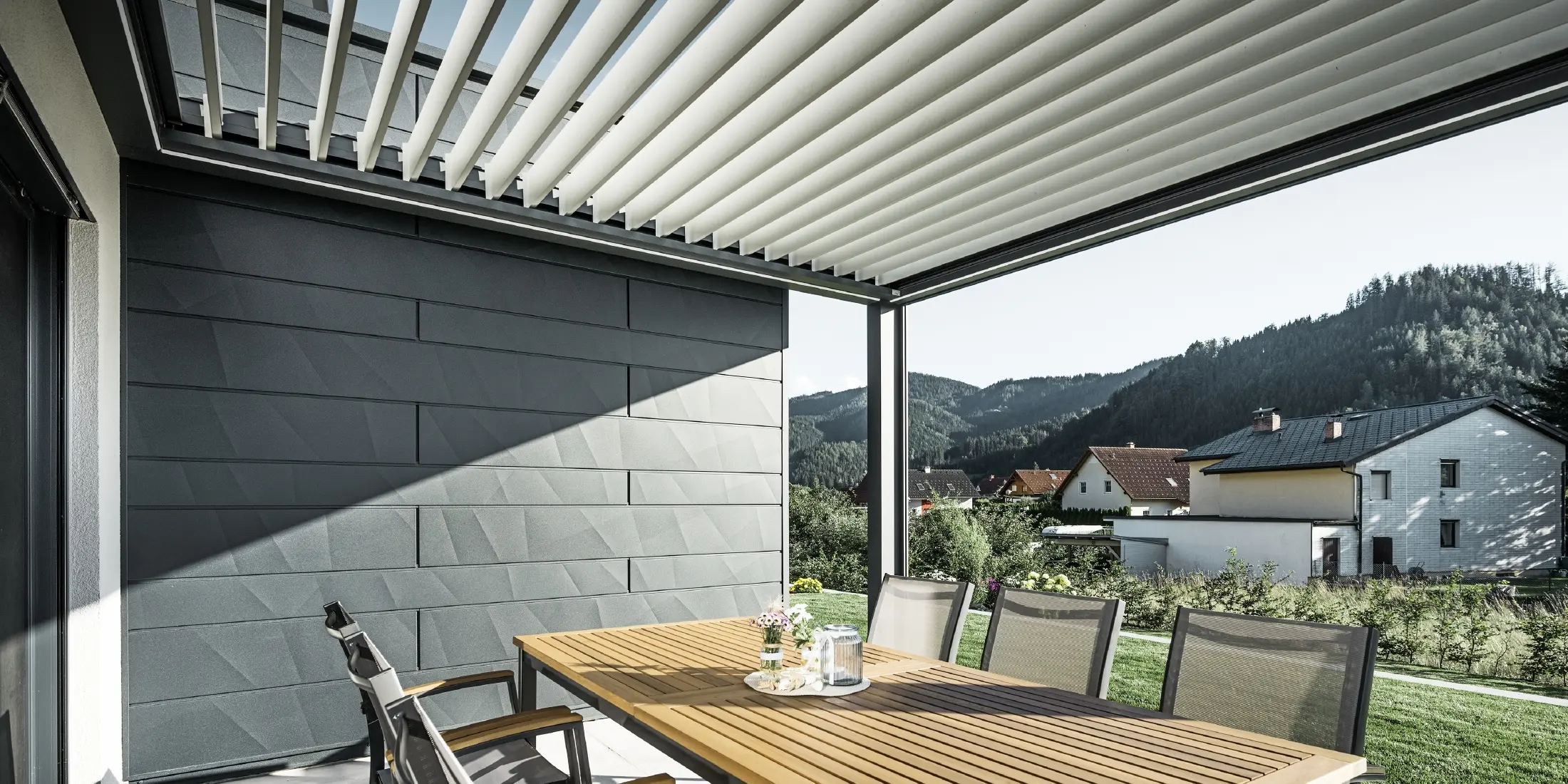 Met lamellen overdekt, beschut terras met tafel en stoelen, een gevelkant is bekleed met de PREFA Siding.X gevelpanelen in antraciet.
