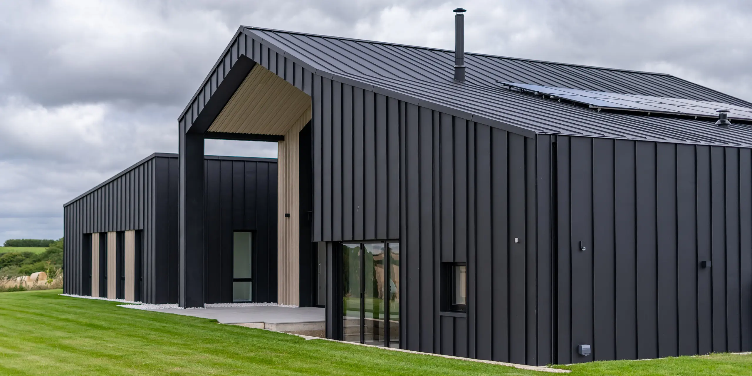 Schrägansicht der Rückseite von ‚The Hide‘ in Cornwall mit PREFALZ Dach- und Fassadenbekleidung in P.10 Anthrazit. Die klare Stehfalzoptik des Daches und der Fassade aus Aluminium erzeugt eine moderne und harmonische Linienführung, die durch Holzelemente und die umgebende Natur ergänzt wird -ein perfektes Zusammenspiel von Funktionalität und Ästhetik.