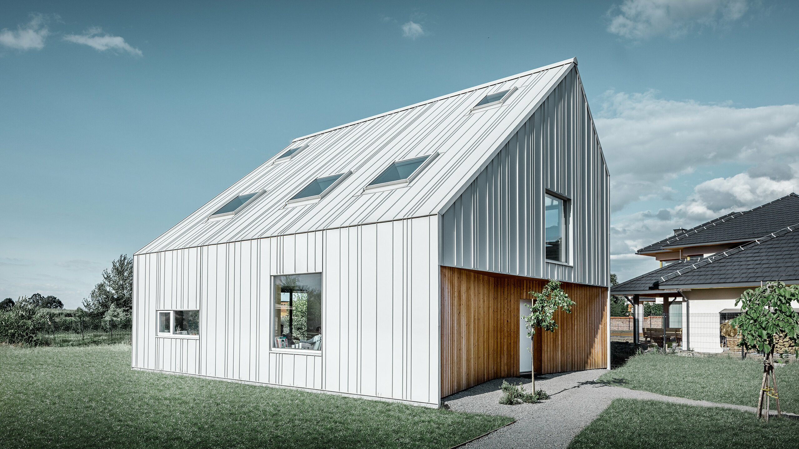 Modern vormgegeven eengezinswoning met zadeldak, de volledige buitenkant is bekleed met PREFALZ in prefawit. Daarbij lopen de verschillend brede panelen van het dak door over de gevel. In het dak bevinden zich verschillende dakvensters.