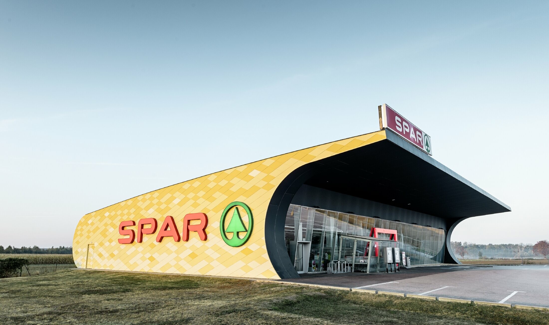 Spar-supermarkt met aluminiumgevel in ruitvormige, geel-oranje composietplaten en Spar-logo