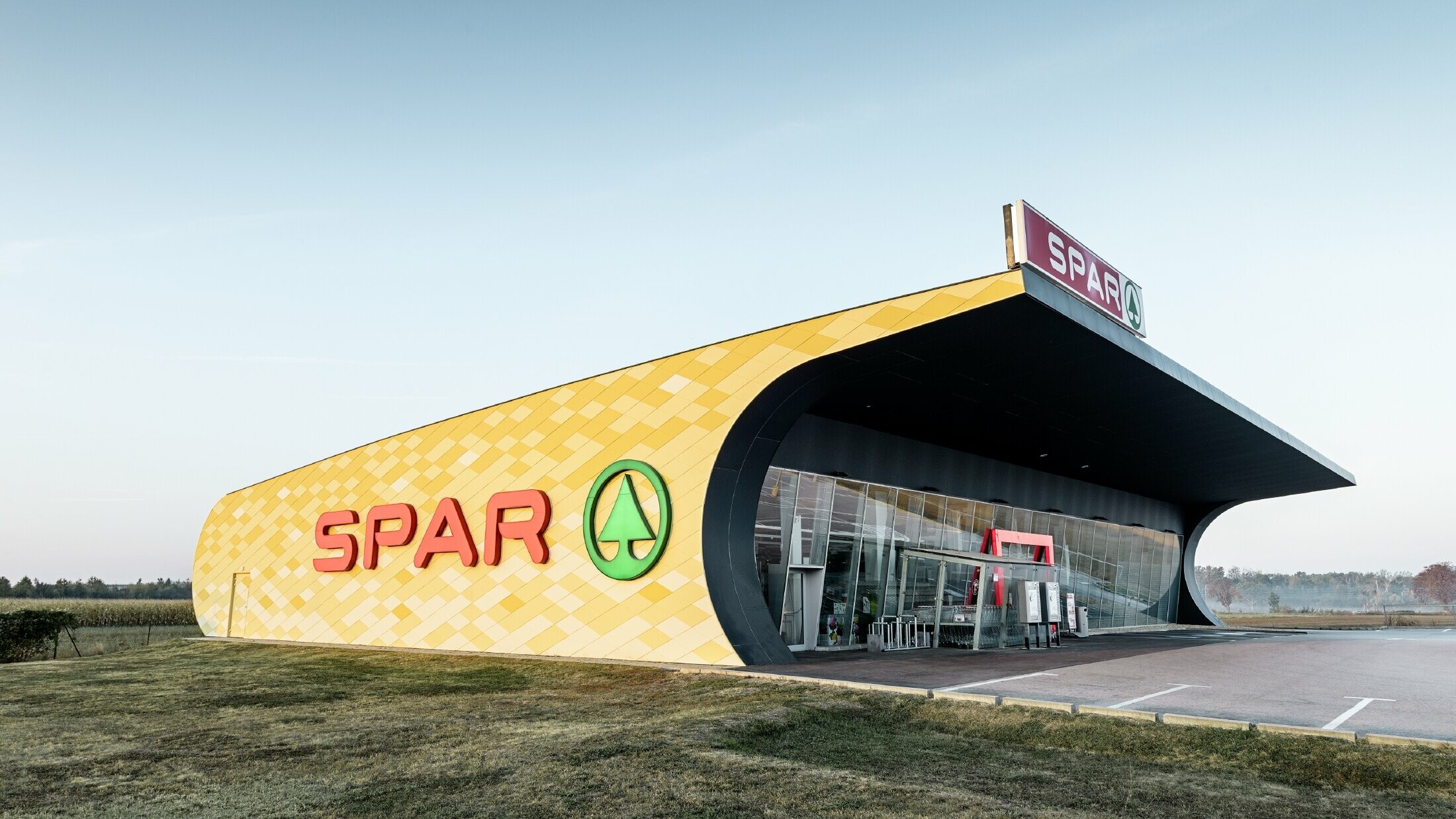 Spar-supermarkt met aluminiumgevel in ruitvormige, geel-oranje composietplaten en Spar-logo