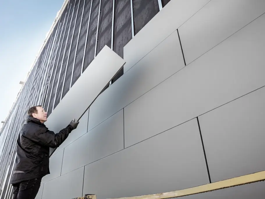 Foto's van een gedeeltelijk afgewerkte gevel, die bekleed is met PREFA Sidings met breedte 500. De dakspecialist plaatst nog een gevelpaneel. De foto is langs onder genomen. 
