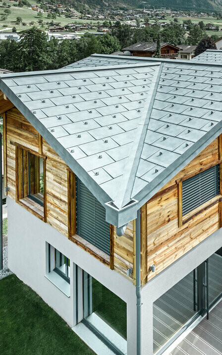 Zwitsers chalet met een aluminium dak van PREFA. Hiervoor is de dakpan R.16 in steengrijs gebruikt. Aan de bovenste etage werd een rustieke houten gevel aangebracht.