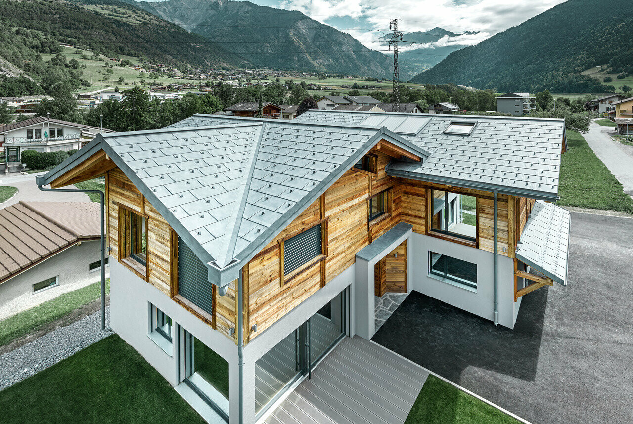 Zwitsers chalet met een aluminium dak van PREFA. Hiervoor is de dakpan R.16 in steengrijs gebruikt. Aan de bovenste etage werd een rustieke houten gevel aangebracht.