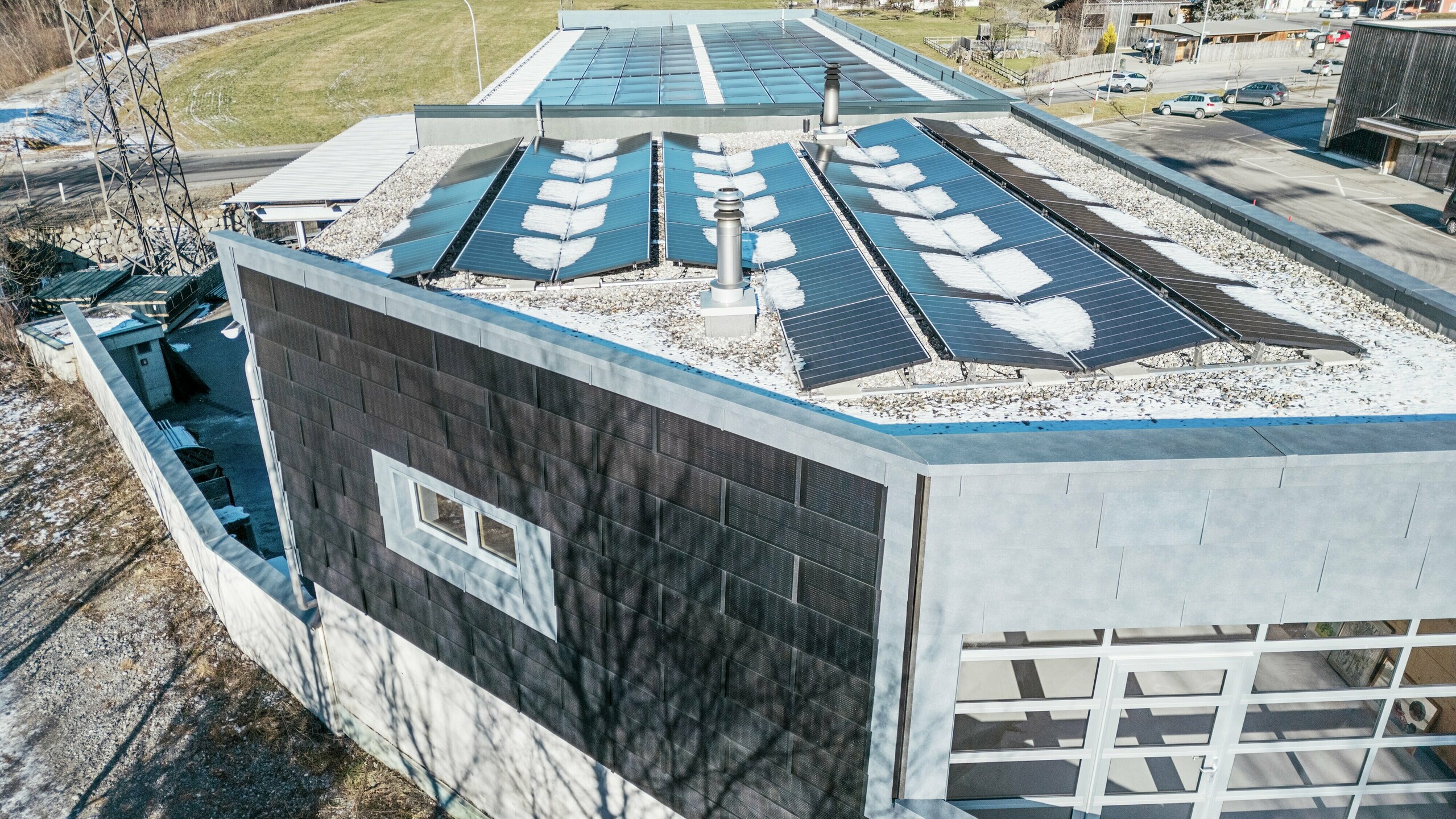 Na slici se iz ptičje perspektive može vidjeti poslovna zgrada tvrtke RÜMA u Vorarlbergu. Na fasadi je postavljena PREFA solarna krovna ploča za održivu proizvodnju električne energije.