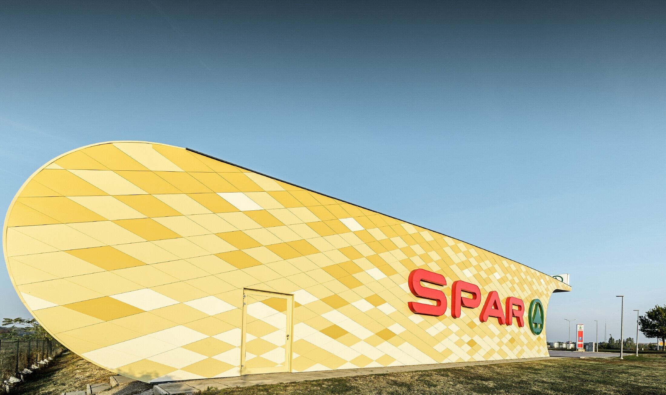 Spar-supermarkt met aluminiumgevel in ruitvormige, geel-oranje composietplaten en Spar-logo