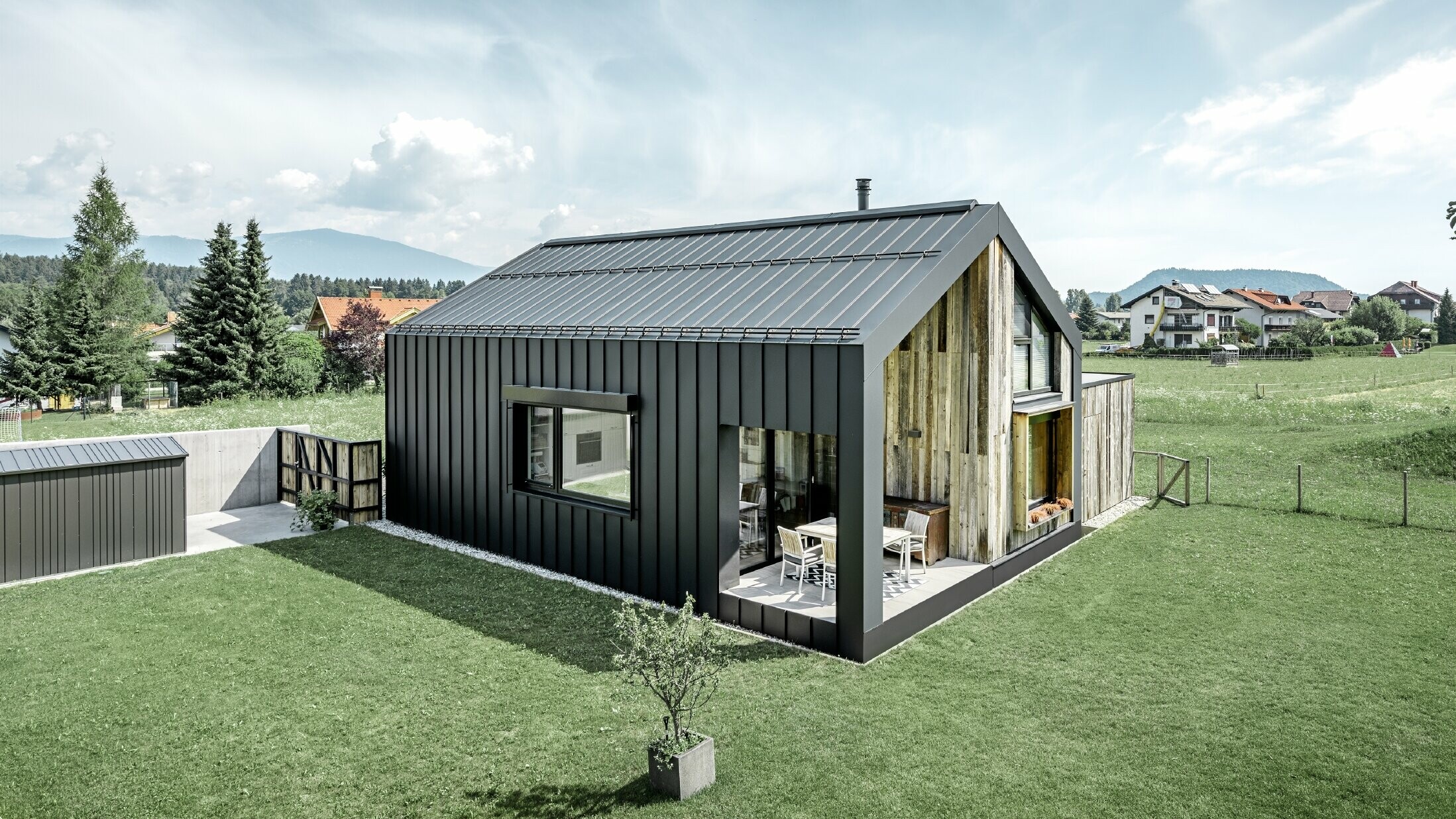 Eengezinswoning met zadeldak, dak- en gevelbedekking met PREFALZ van PREFA in P.10 antraciet. De panelen van het dak lopen door over de gevel. Een deel van de gevel is bekleed met verweerd hout.