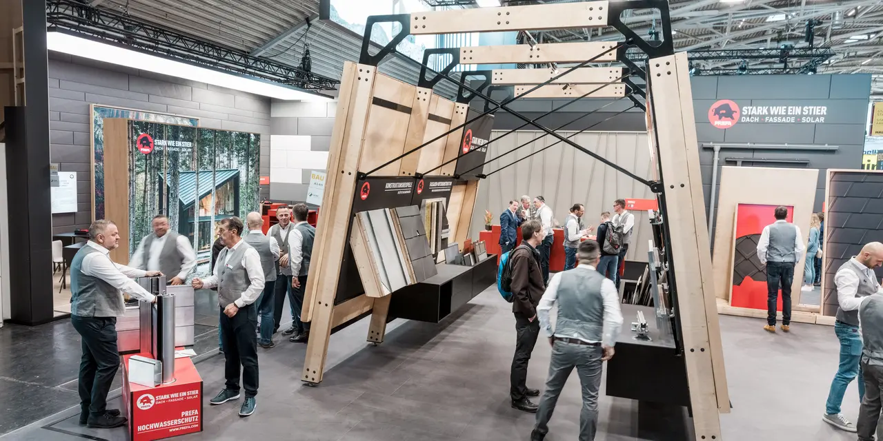 Drukbezochte PREFA-beursstand met beurswanden waarop de PREFA-dak- en gevelproducten van aluminium te zien zijn.
