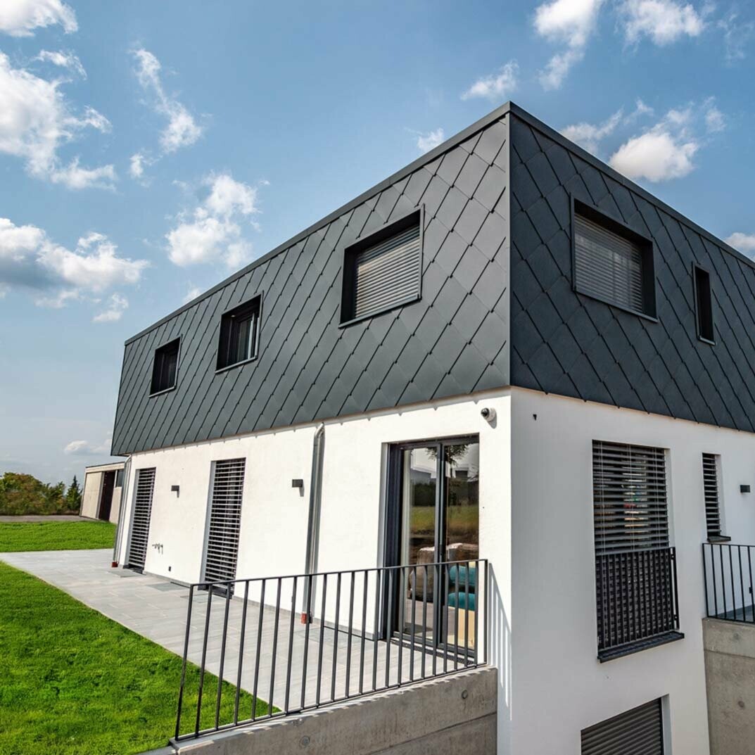 Moderne nieuwbouw met plat dak - de gevel van de bovenverdieping is bekleed met de PREFA aluminium gevellosange van 44 × 44 in antraciet. Het onderste geveldeel is wit gestuct.