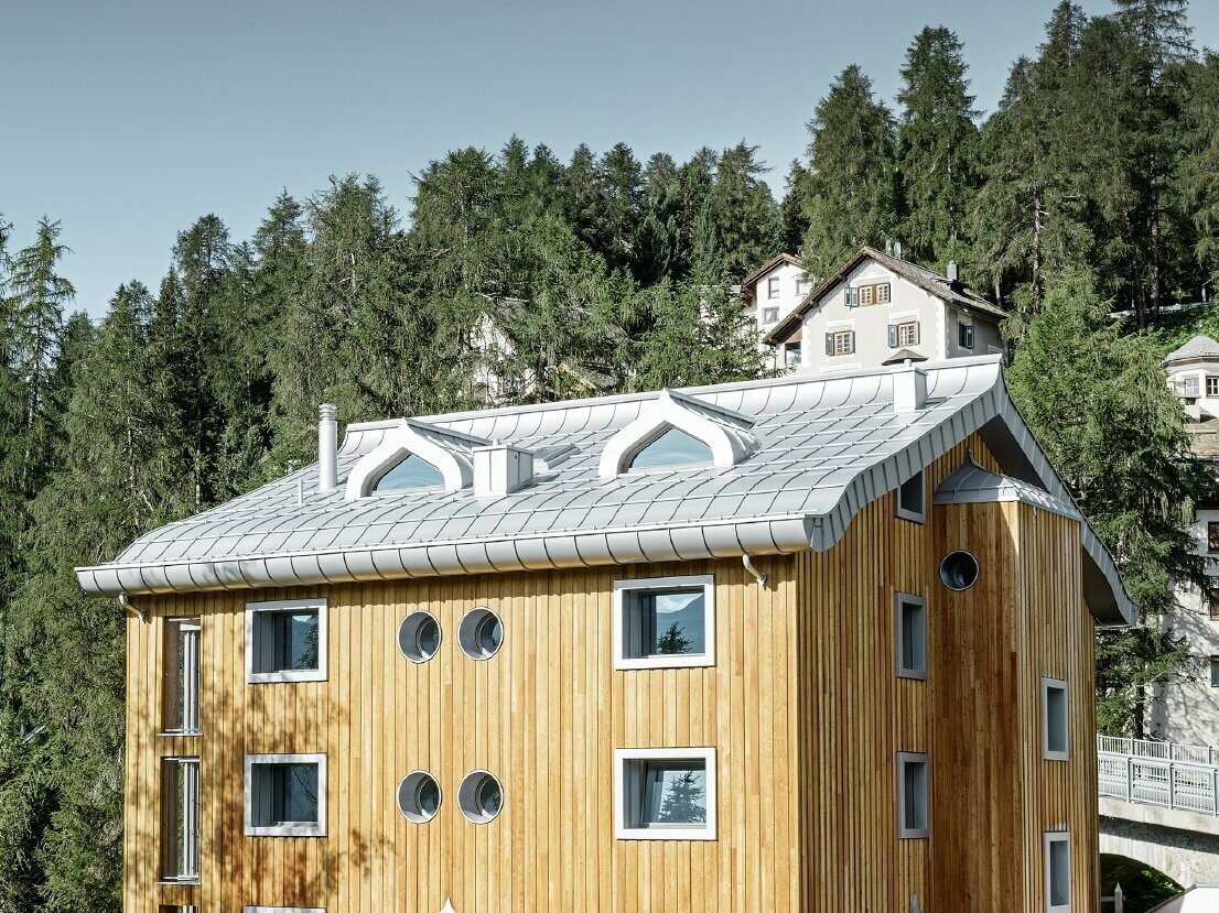 Meergezinswoning in Sankt Moritz (Zwitserland) met houten gevel en aluminiumdak met gekromde dakrand in zilver metallic