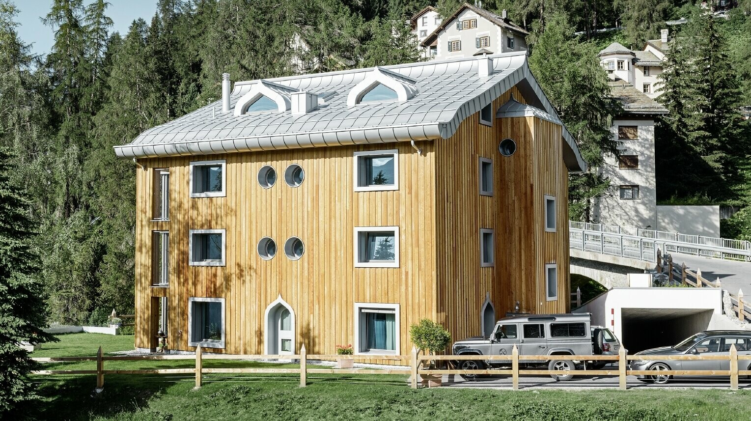Meergezinswoning in Sankt Moritz (Zwitserland) met houten gevel en aluminiumdak met gekromde dakrand in zilver metallic