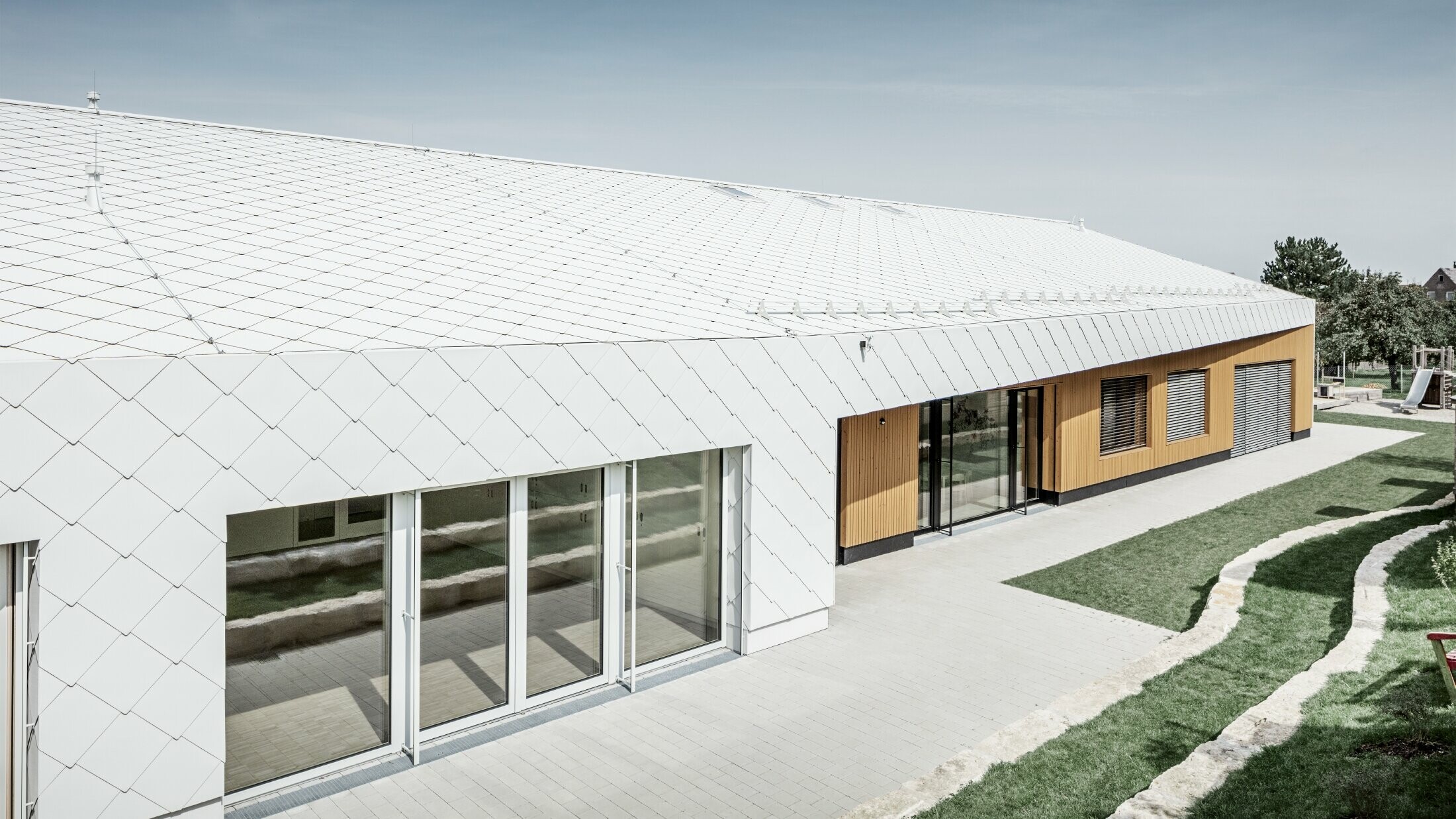 Kleuterschool bekleed met PREFA dak- en gevellosanges 44 in prefawit, het dakoppervlak loopt door over de gevel; grote raampartijen