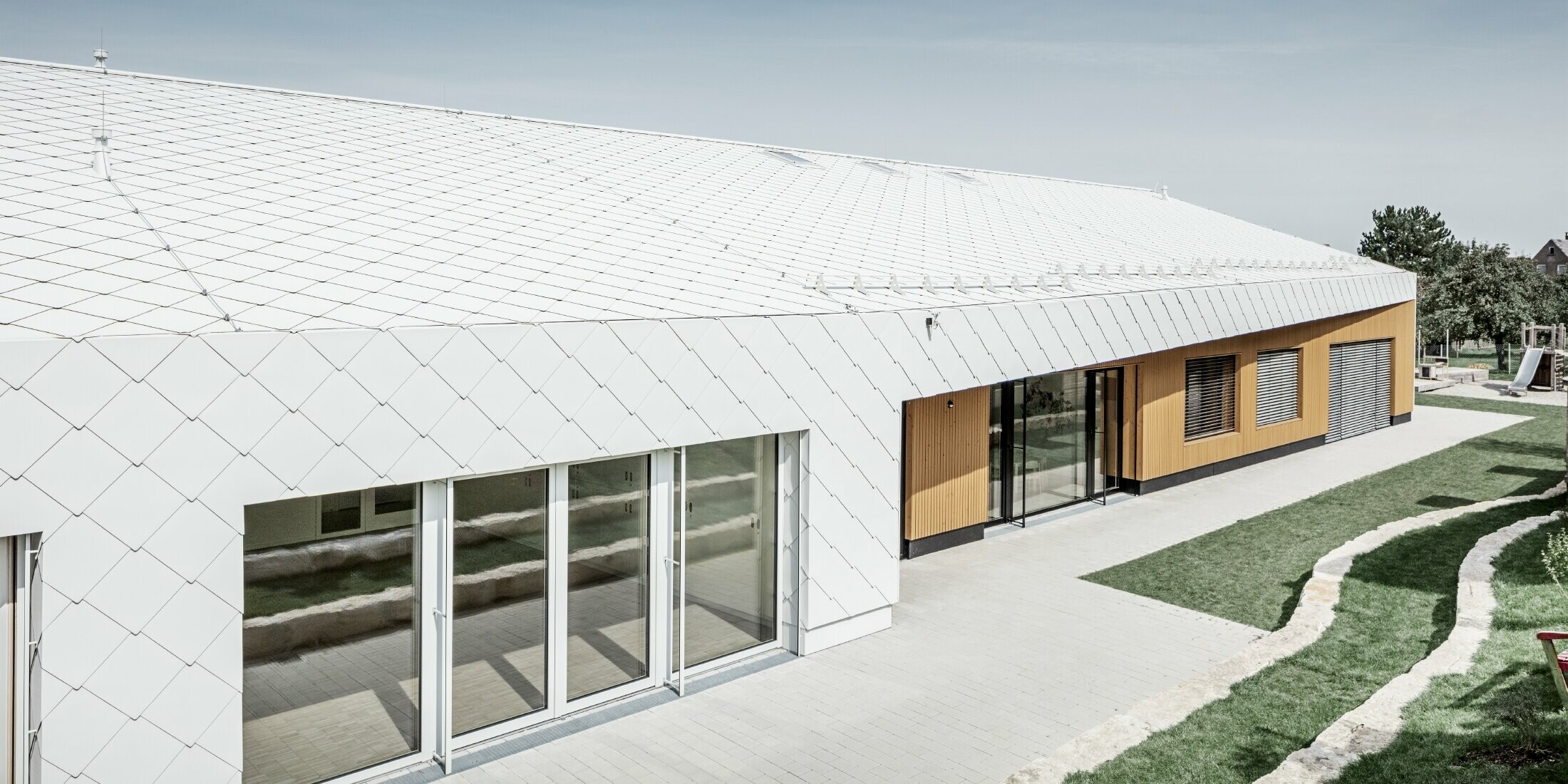 Kleuterschool bekleed met PREFA dak- en gevellosanges 44 in prefawit, het dakoppervlak loopt door over de gevel; grote raampartijen