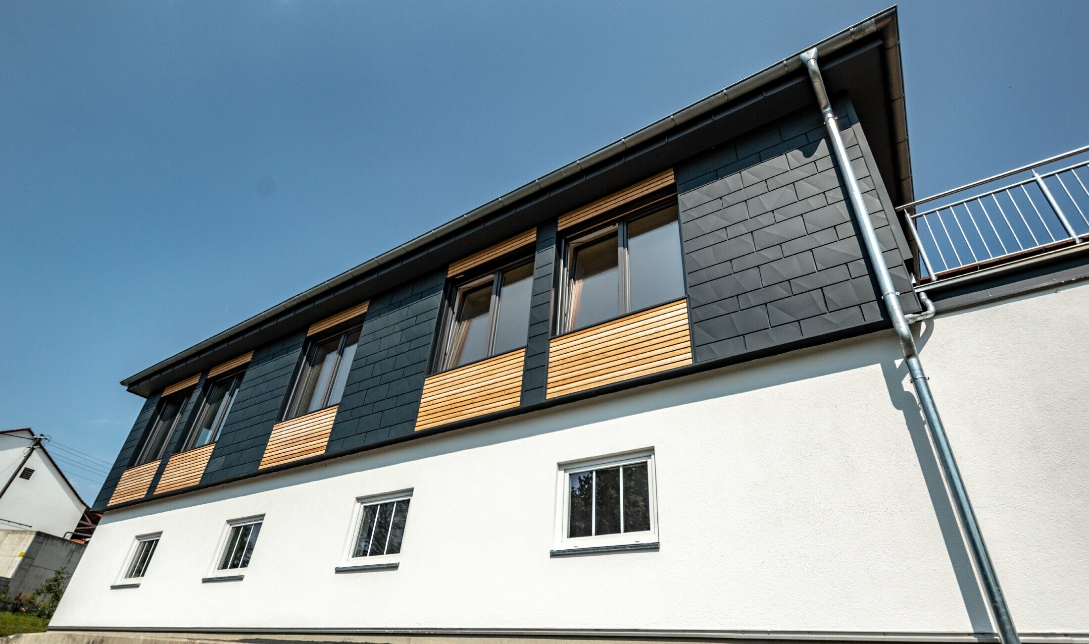 Gevelvormgeving met verschillende bouwmaterialen: gebruikt werden aluminium PREFA Siding.X in antraciet, een horizontale houten gevel en een wit gestucte gevel.