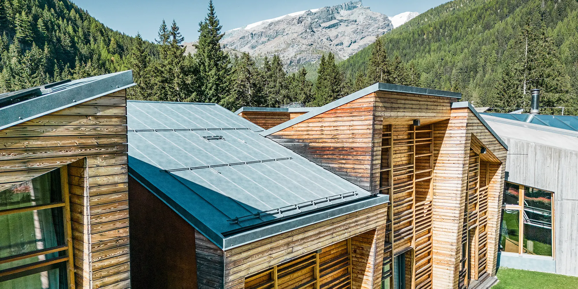 Seitliche Detailansicht der Dachlandschaft, die Holzfassade und die sorgfältig verlegten Prefalz Bahnen sind gut sichtbar.