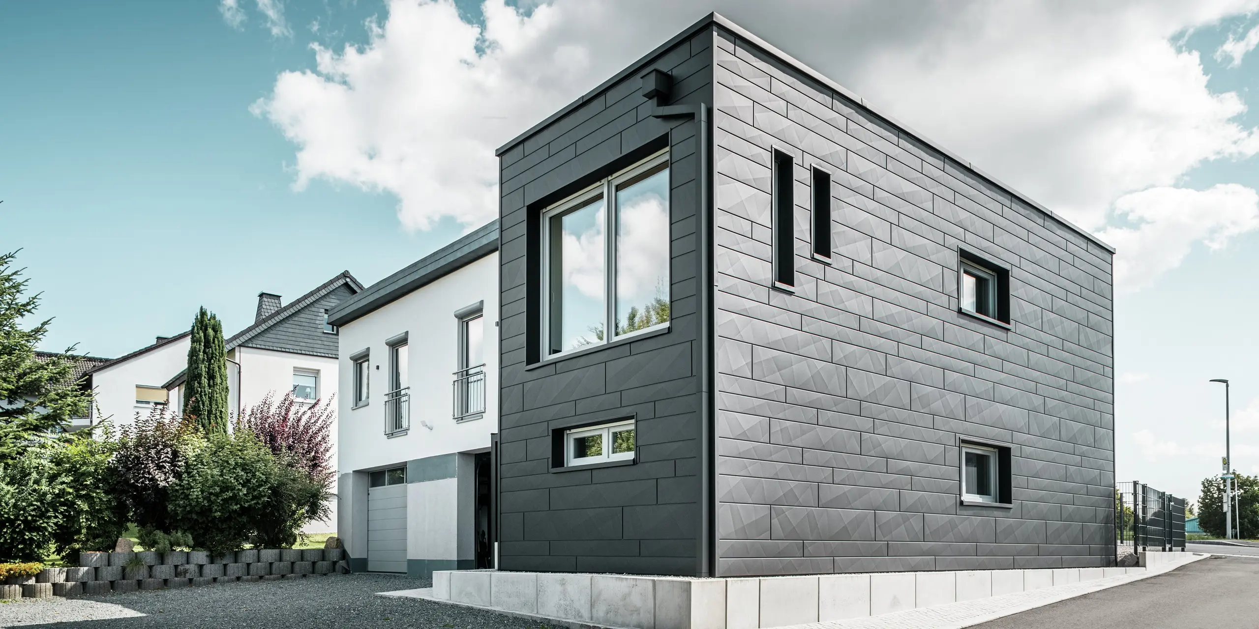 De stijlvolle en moderne gevel van de gerenoveerde eengezinswoning in Teuschnitz is voorzien van de duidelijk gestructureerde PREFA Siding.X-panelen in P.10 zwart. De geometrische opstelling van de hoogwaardige plaatpanelen geeft het gebouw een opvallende, tijdloze uitstraling. De ramen zijn omlijst met zwarte aluminium composietplaten, wat het ontwerp harmonieus afrondt. De geïntegreerde PREFA dakafvoersystemen met vierkante buis zorgen voor een functionele en esthetische oplossing.