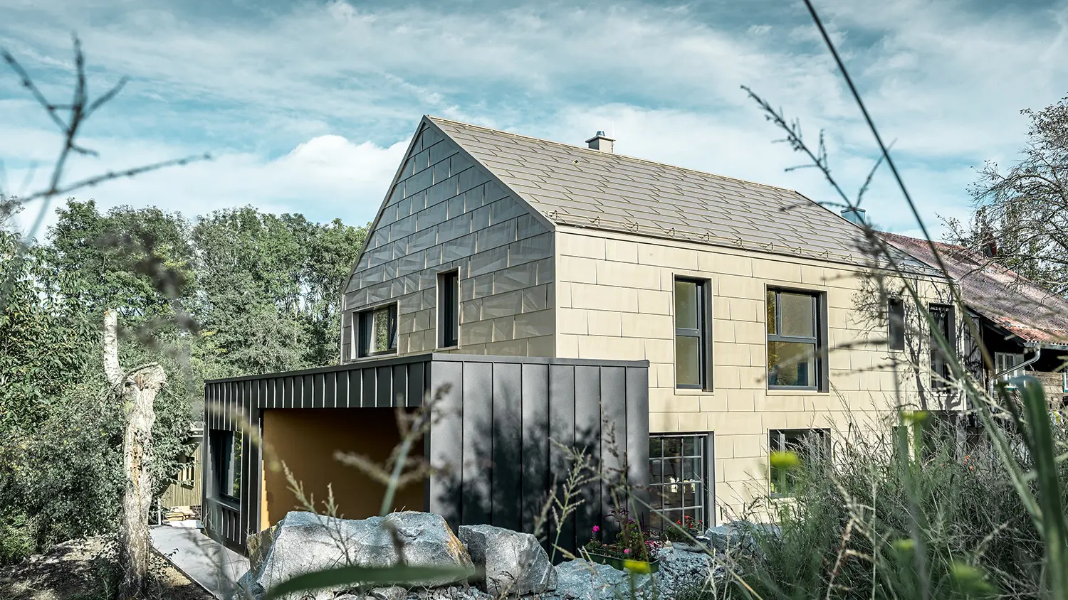 Woonhuis zonder dakoversteek is op het dak en de gevel bekleed met het aluminium paneel FX.12 van PREFA in brons. Vlak daarnaast staat een garage met plat dak met een gevel met staande hoeknaad.