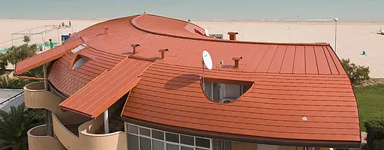Afgerond dak van een wooncomplex bedekt met PREFA-dakschindel en roevendak (Prefalz) van PREFA in baksteenrood.
