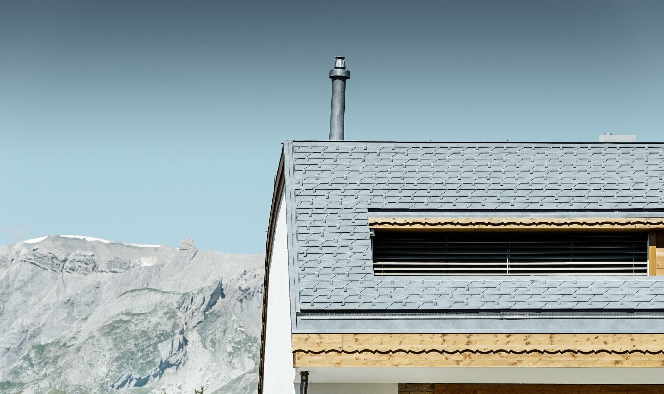 Meergezinswoning in Crans Montana (Zwitserland) met de bergen als decor, een gevel met speelse houten elementen en een dakbedekking bestaande uit aluminium PREFA-dakschindels in steengrijs