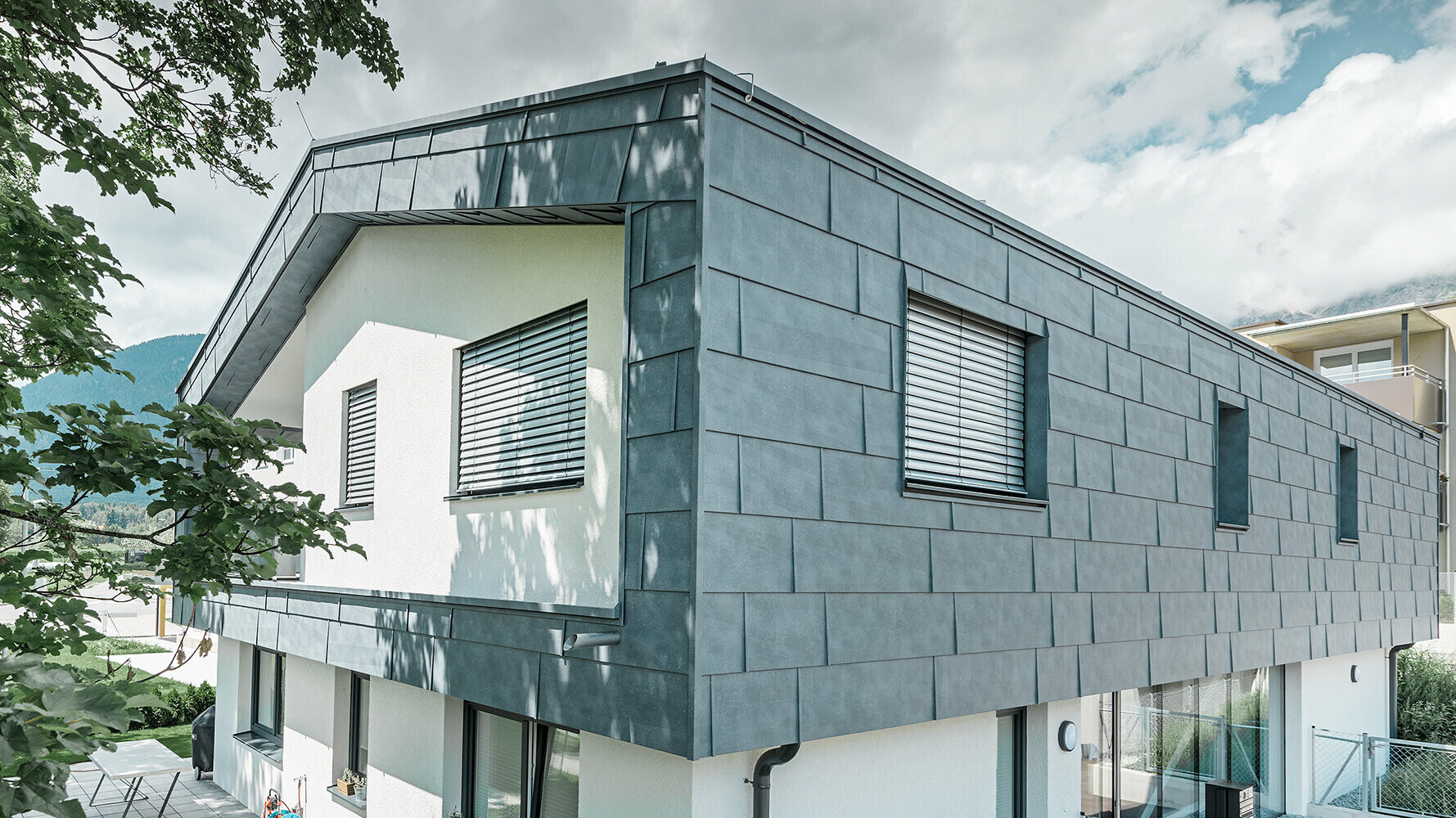 Moderne eengezinswoning zonder dakoverstek; de bovenverdieping is bedekt met PREFA-gevelpanelen FX.12 in steengrijs, de rest van de gevel is wit gestuukt.