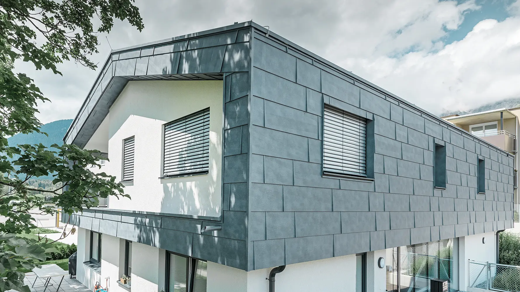 Moderne eengezinswoning zonder dakoverstek; de bovenverdieping is bedekt met PREFA-gevelpanelen FX.12 in steengrijs, de rest van de gevel is wit gestuukt.