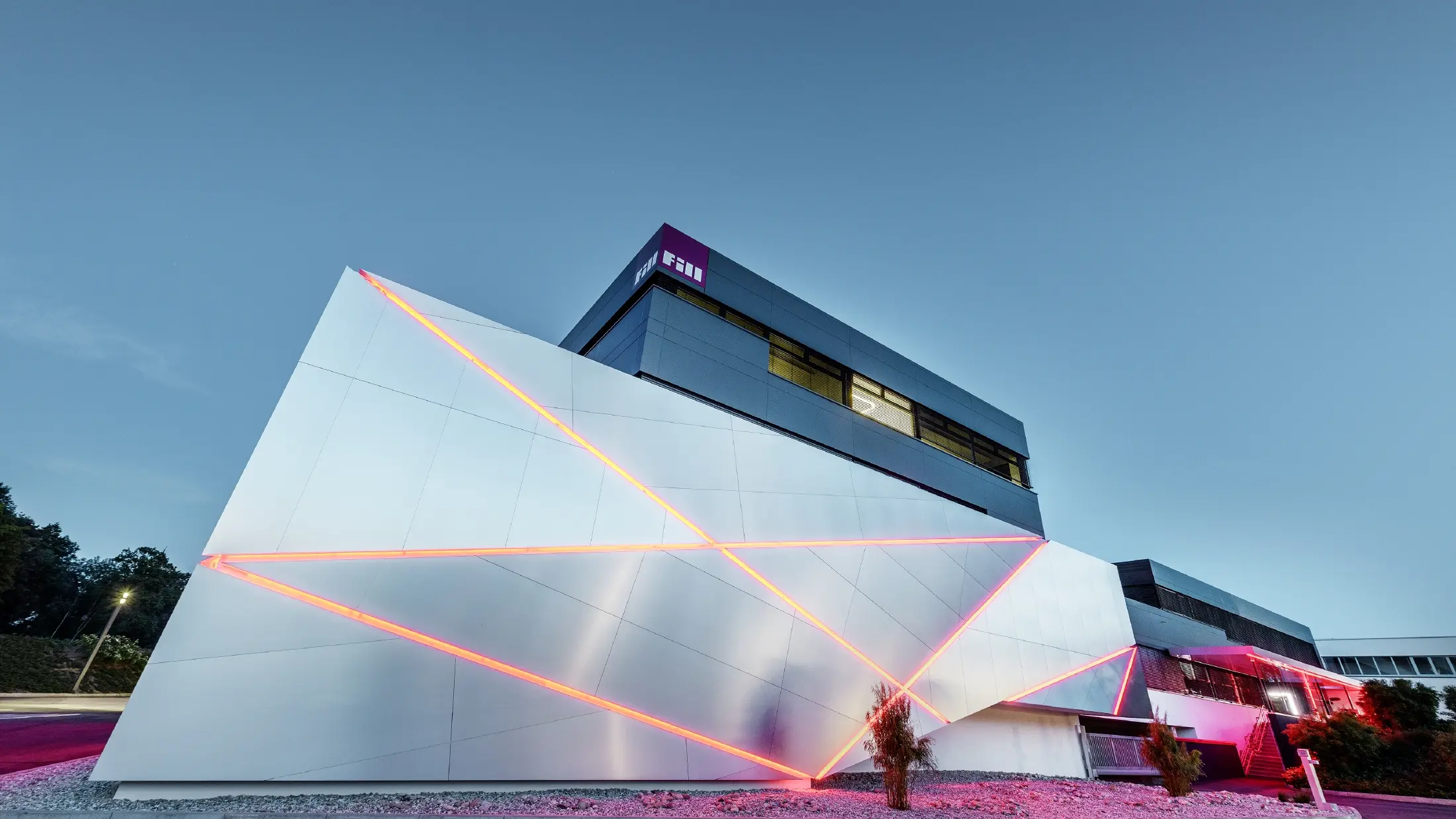 Bedrijfsgebouw (Fill) met futuristische gevel met composietplaten in geborsteld aluminium en achtergrondverlichting in de voegen.