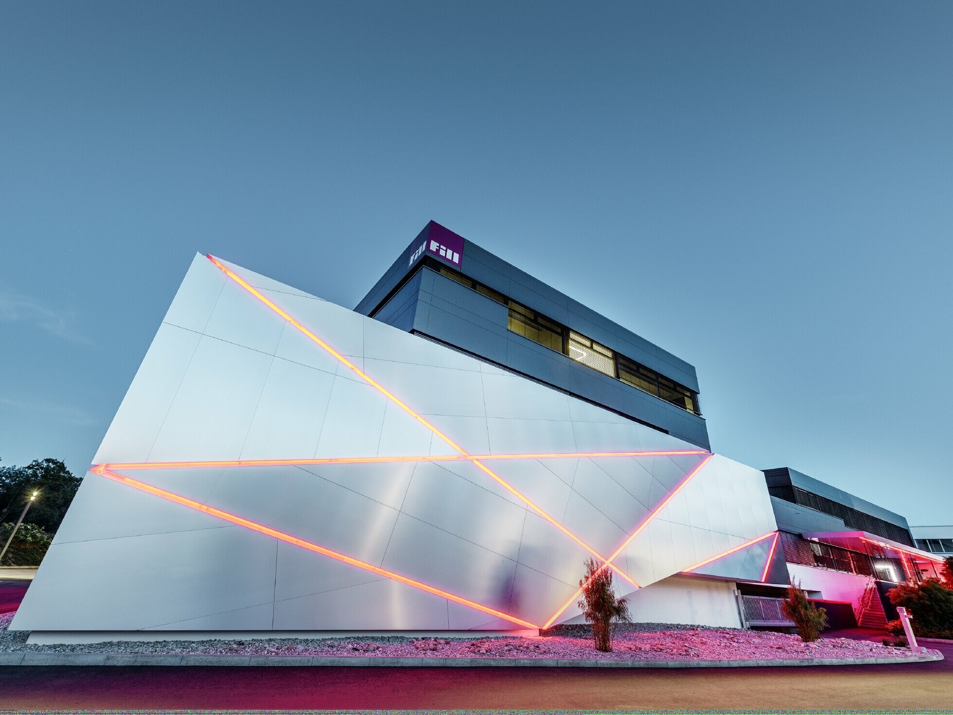 Bedrijfsgebouw (Fill) met futuristische gevel met composietplaten in geborsteld aluminium en achtergrondverlichting in de voegen.