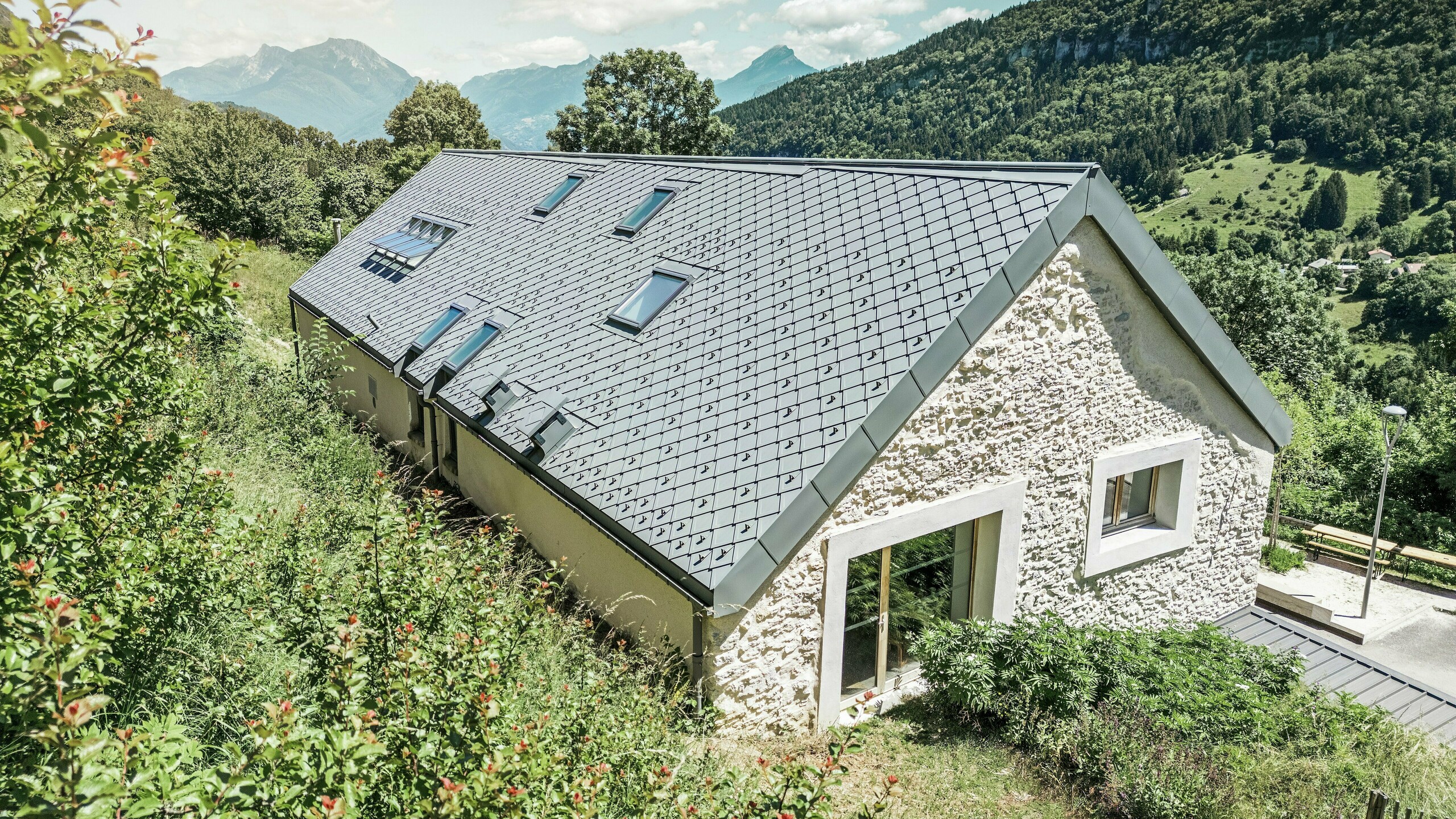 Dachansicht der sanierten Scheune "La Grange à Gaby" in Engins, Frankreich. Das Gebäude ist mit langlebigen PREFA 29 × 29 Dachrauten gedeckt, die modernen Schutz mit traditioneller Ästhetik verbinden. Die idyllische Berglandschaft unterstreicht die harmonische Einbindung in die Natur.