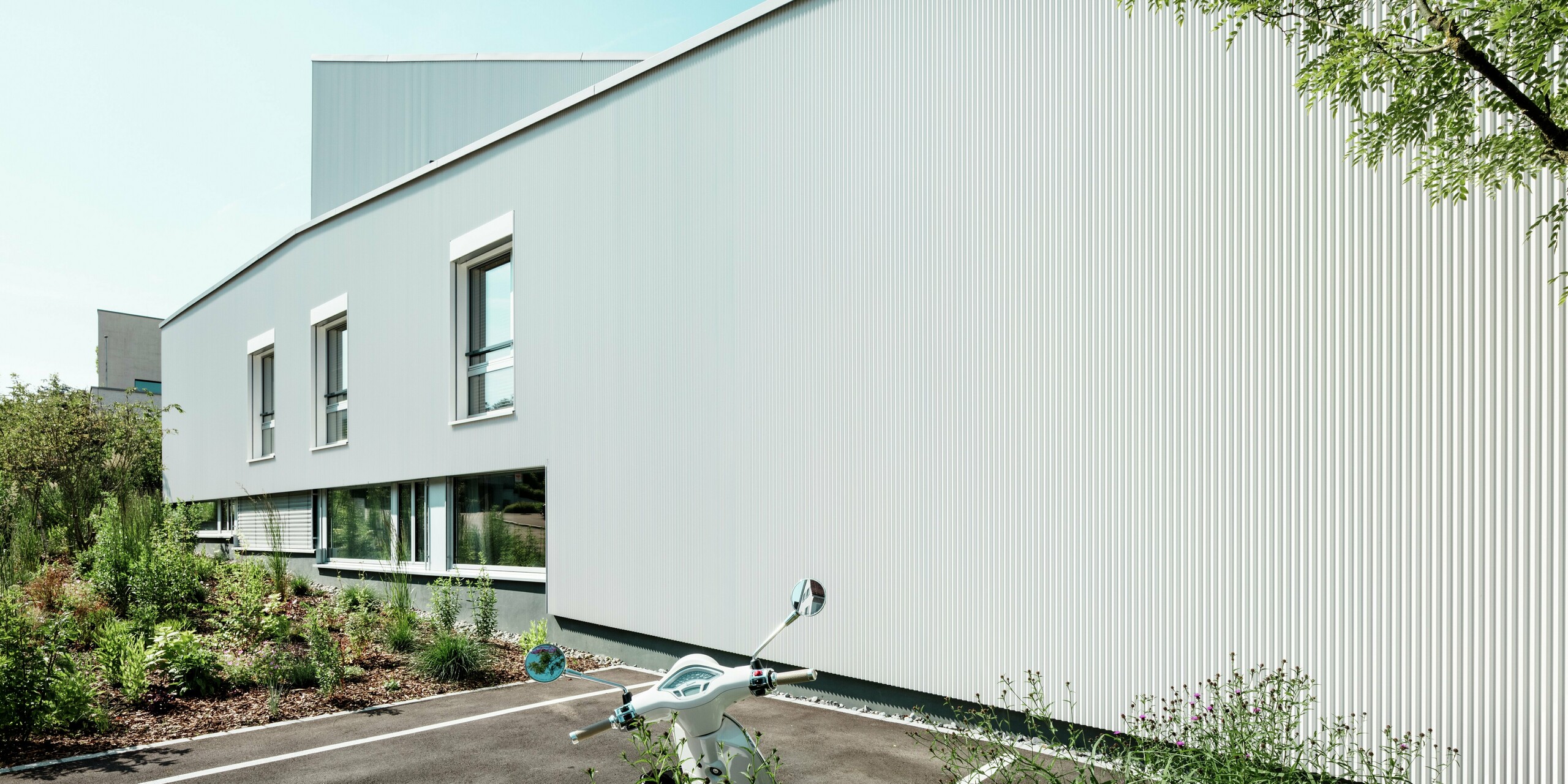 Klare Linien und minimalistisches Design prägen die Fassade der Tiny Homes am Zollikerberg mit PREFA Zackenprofil und Aluminium Verbundplatten in P.10 Reinweiß. Die feine Struktur der Zacken erzeugt ein lebendiges Lichtspiel, während das langlebige Aluminium optimalen Witterungsschutz bietet. Der moderne Look wird durch reduzierte Fenster und die elegante Flucht der Flächen unterstrichen.