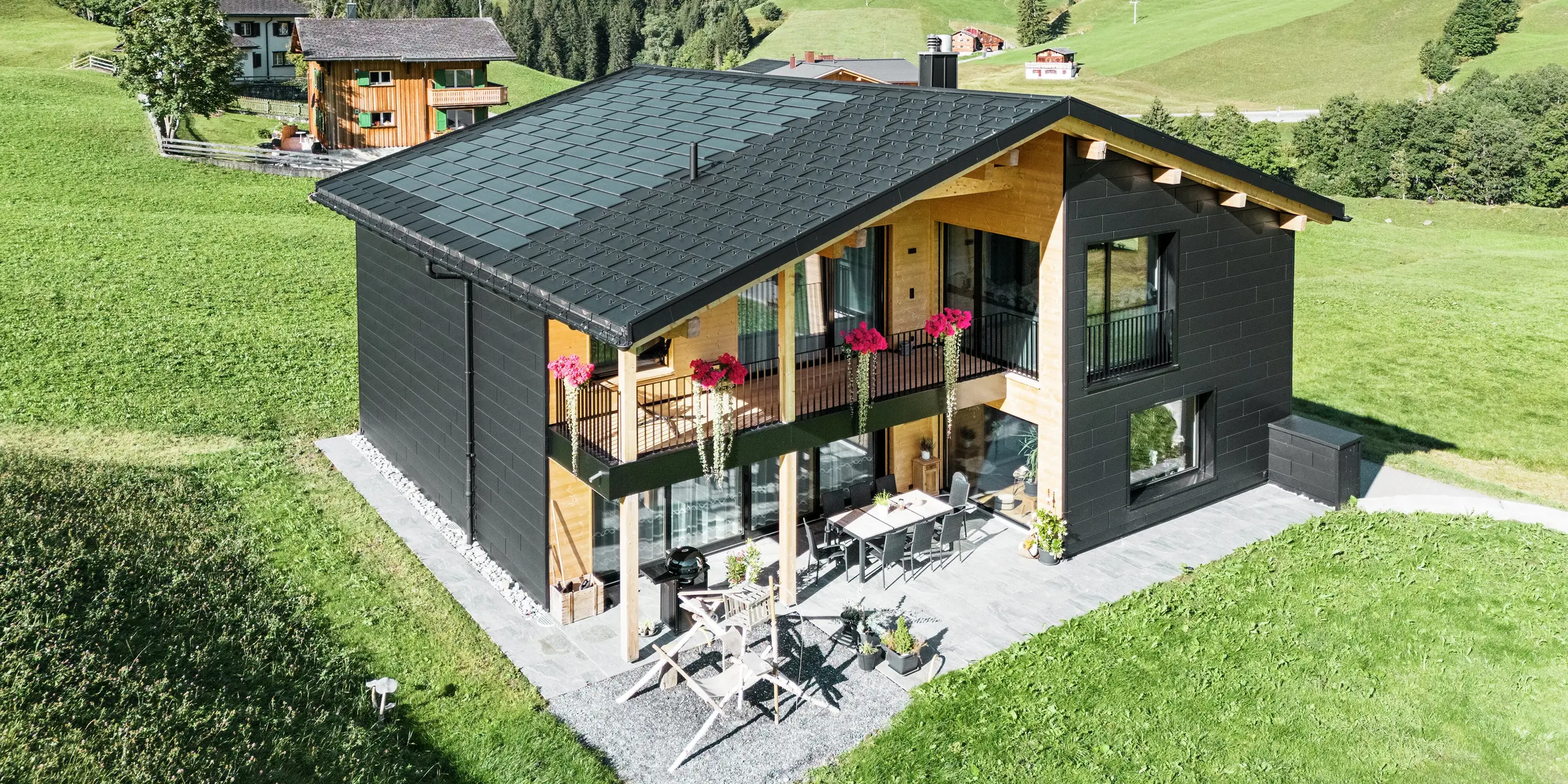 Het elegante vrijstaande huis in de heuvelachtige omgeving van Ascharina (Zwitserland) laat zien hoe aluminium en hout perfect gecombineerd kunnen worden. De robuuste PREFA Siding.X gevelplaten in P.10 zwart harmoniëren met het dak van PREFA Solar dakplaten en R.16 dakplaten in dezelfde kleurcoating. De duurzame aluminium gevelbekleding beschermt het gebouw betrouwbaar tegen de uitdagingen van het alpine klimaat.