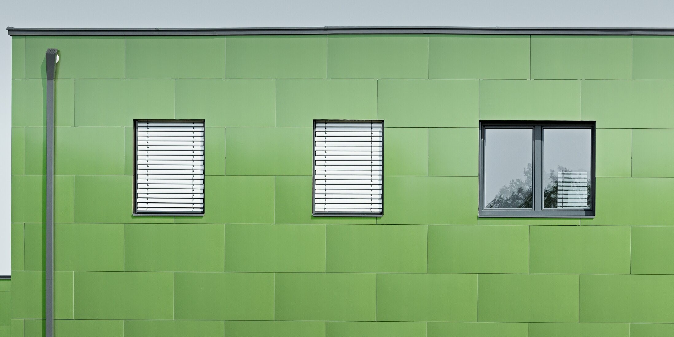 Vooraanzicht van de aluminium composietplaat van PREFA met kameleonlook en wisselende kleuren. Helemaal links ziet u de hoekige afvoerbuis, de vierkante buis van PREFA