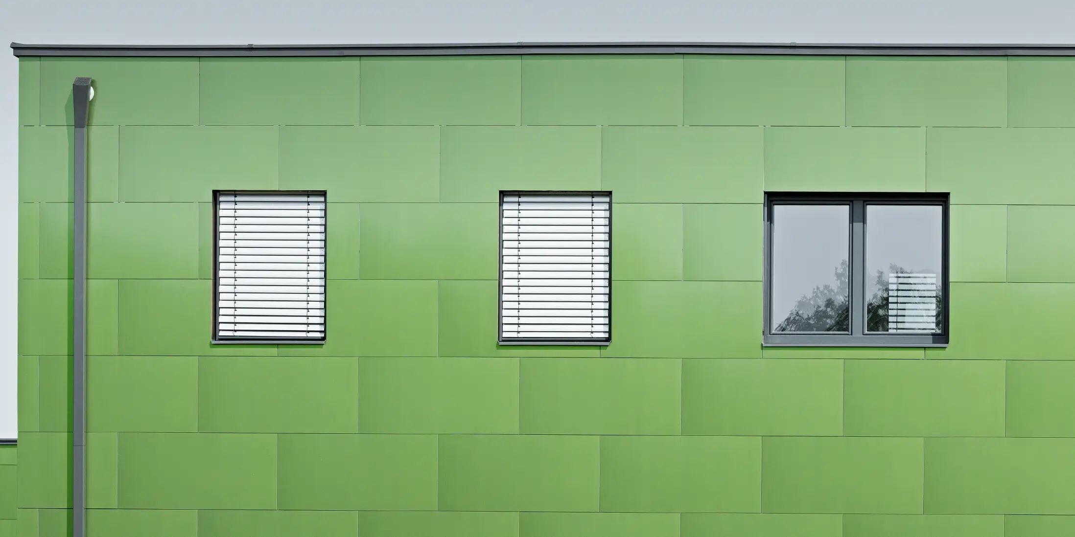 Vooraanzicht van de aluminium composietplaat van PREFA met kameleonlook en wisselende kleuren. Helemaal links ziet u de hoekige afvoerbuis, de vierkante buis van PREFA