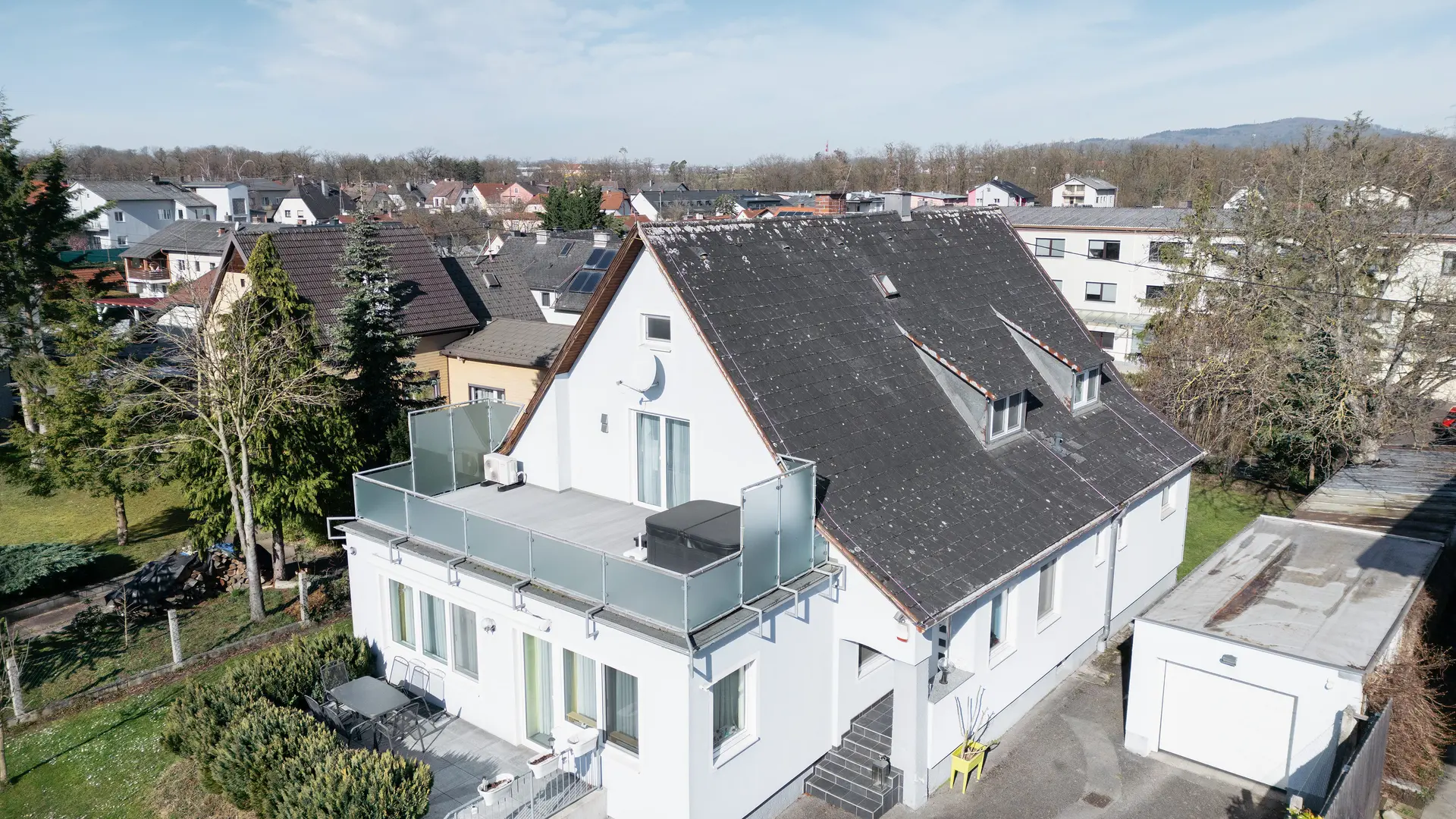 Vogelvluchtperspectief op een gebouw met een oud eternietdak dat bedekt is met vuil en korstmossen. Er zijn geen zonnepanelen op het dak te zien. Het balkon op de voorgrond heeft een glazen balustrade en bevindt zich op de bovenste verdieping van het gebouw.