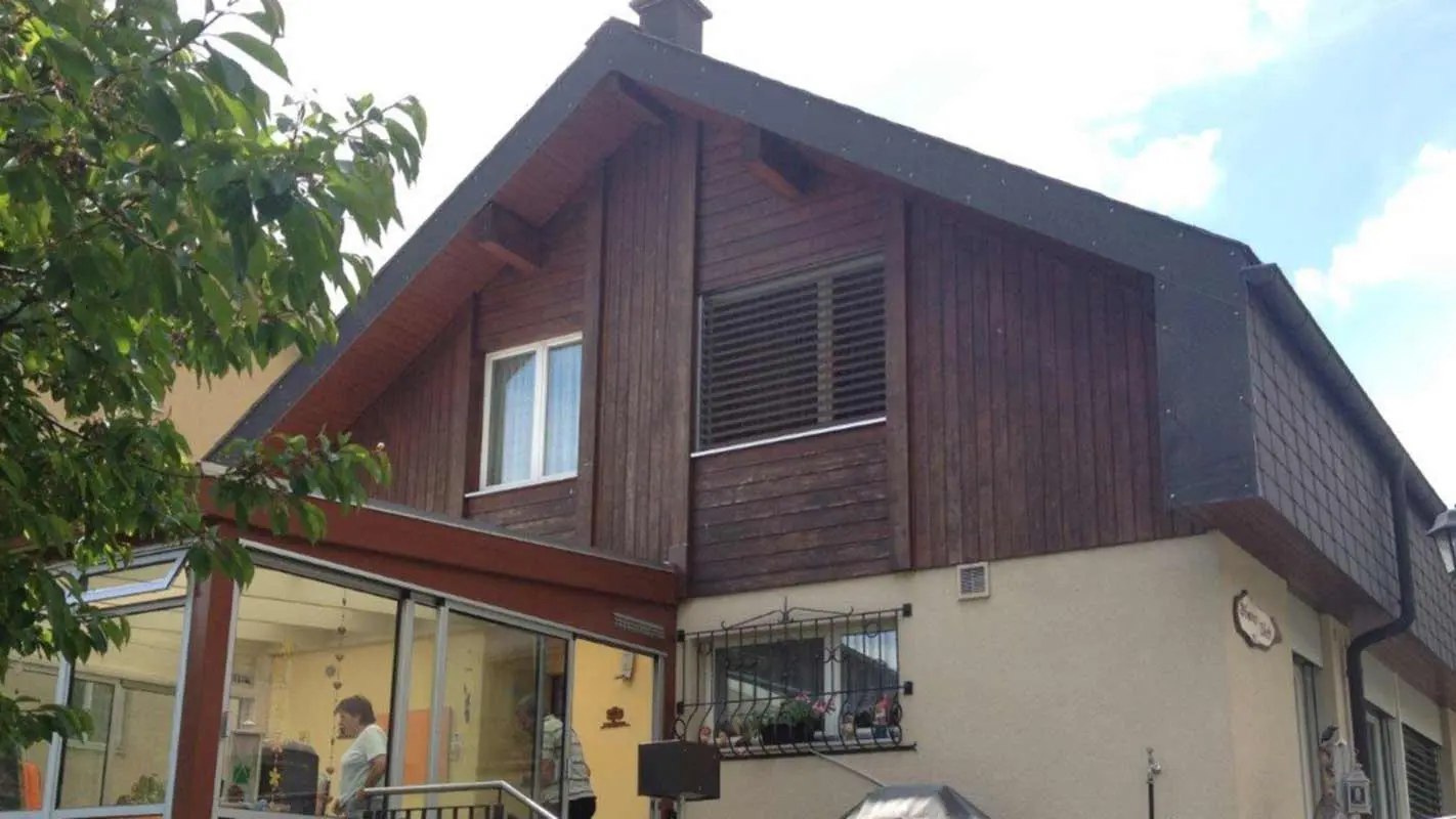 Huis voor de gevelrenovatie met PREFA gevelbeplating in hout-look, topgevel is momenteel bekleed met verweerd hout