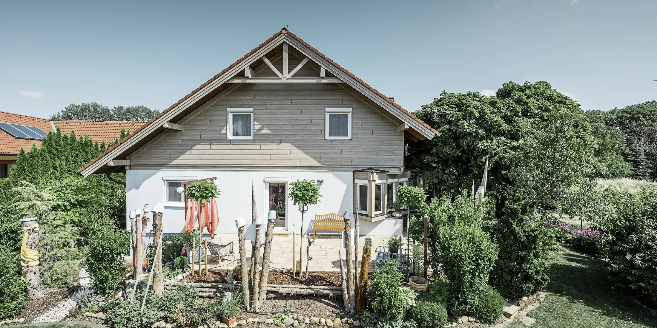Eengezinswoning met gerenoveerde gevel en vernieuwde gevelbekleding in een moderne houtlook in grijs-beige, gecombineerd met een gepleisterde gevel, een zadeldak en een goed onderhouden tuin.
