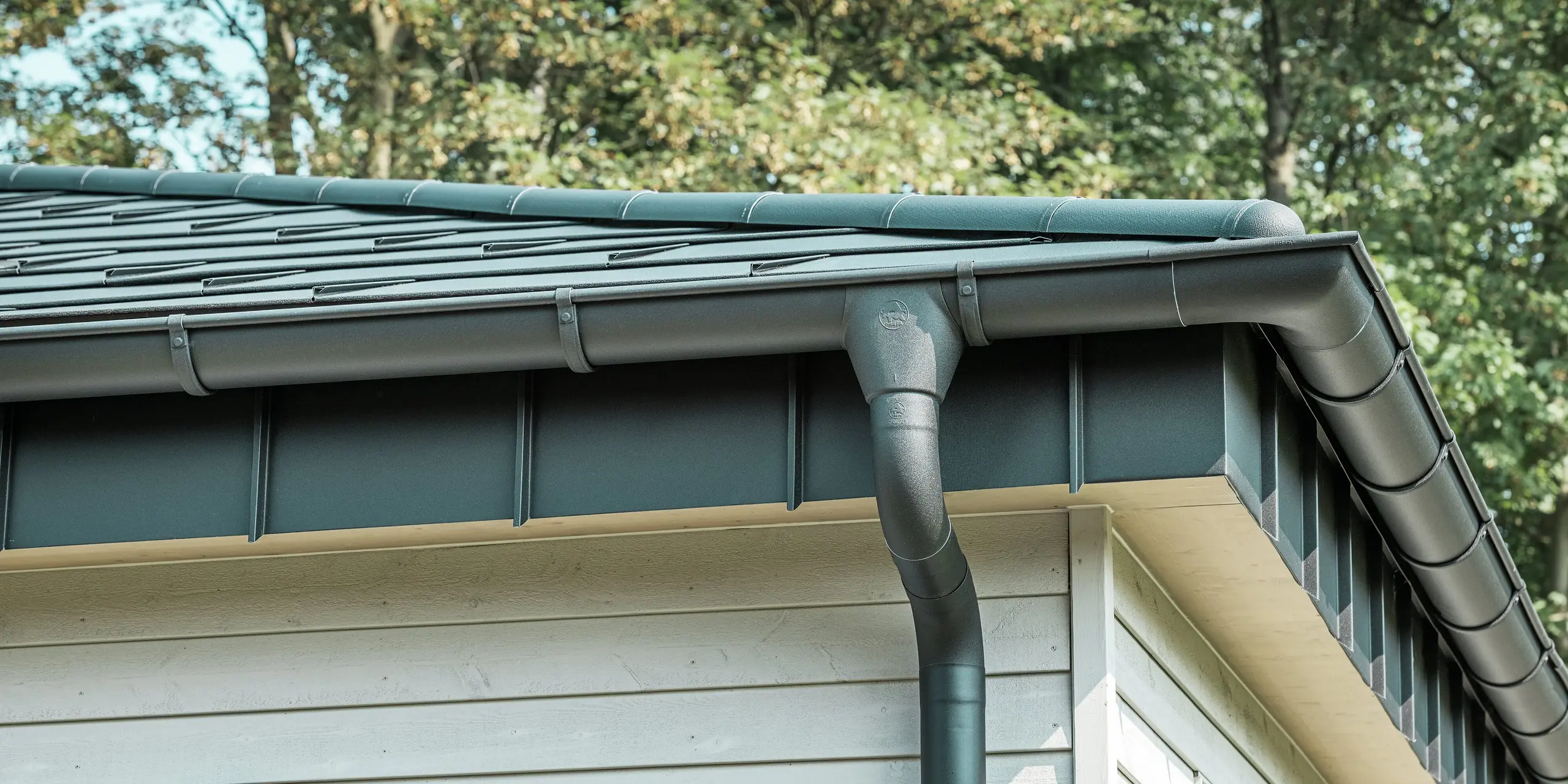 Detailaanzicht van het PREFA dakafvoersysteem van een bungalow in Rommerskirchen. De hoogwaardige ardense goot en de afvoerbuis in P.10 zwart zorgen voor een veilige afvoer van het regenwater. De duurzame PREFA aluminiumproducten combineren functionaliteit met een modern, elegant design.