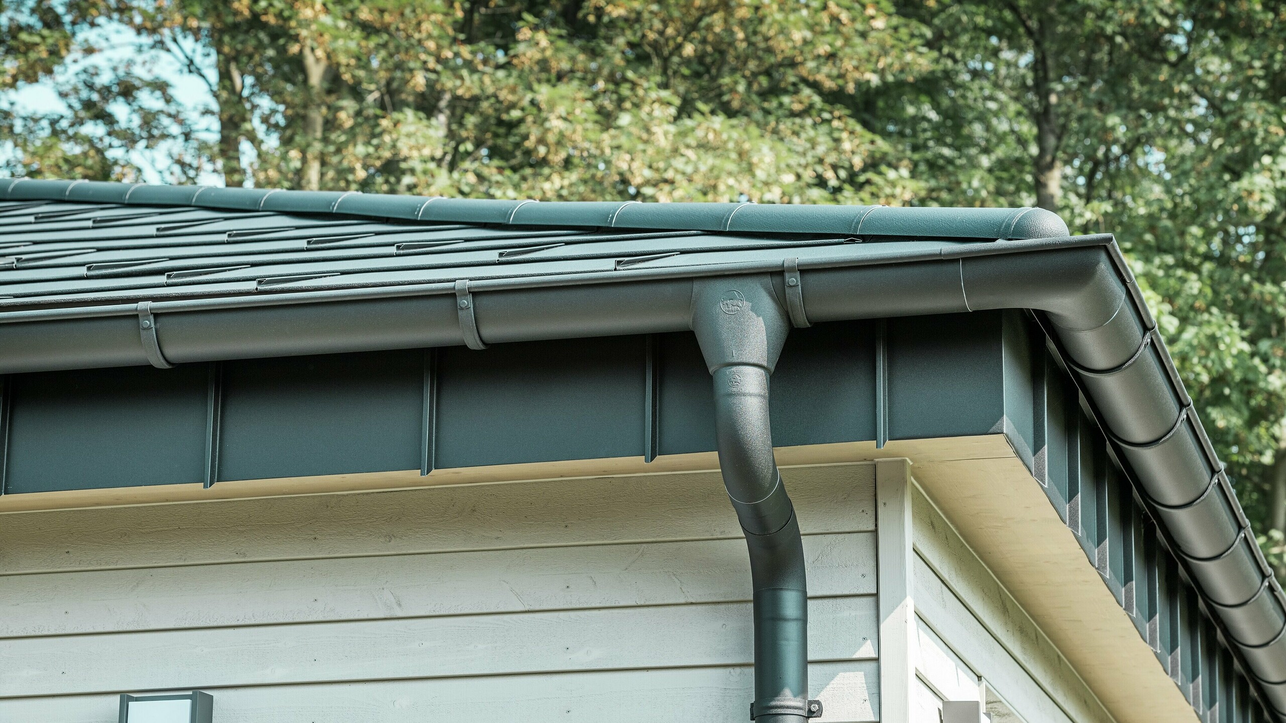 Detailaanzicht van het PREFA dakafvoersysteem van een bungalow in Rommerskirchen. De hoogwaardige ardense goot en de afvoerbuis in P.10 zwart zorgen voor een veilige afvoer van het regenwater. De duurzame PREFA aluminiumproducten combineren functionaliteit met een modern, elegant design.