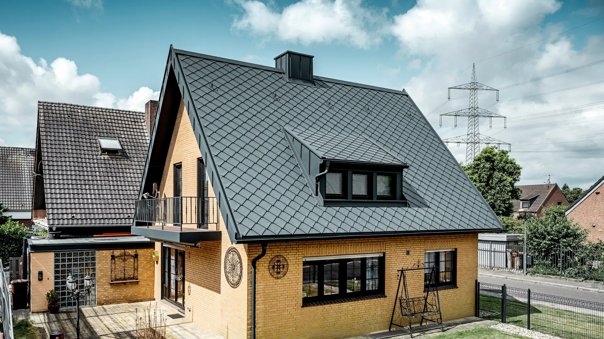 Eengezinswoning van gele baksteen na de dakrenovatie met PREFA daklosangen 29 × 29 in donkergrijs; nieuw bedekt, steil zadeldak met ruitpatroon, geïntegreerde dakkapel en schoorsteen, terras en tuin op de voorgrond.