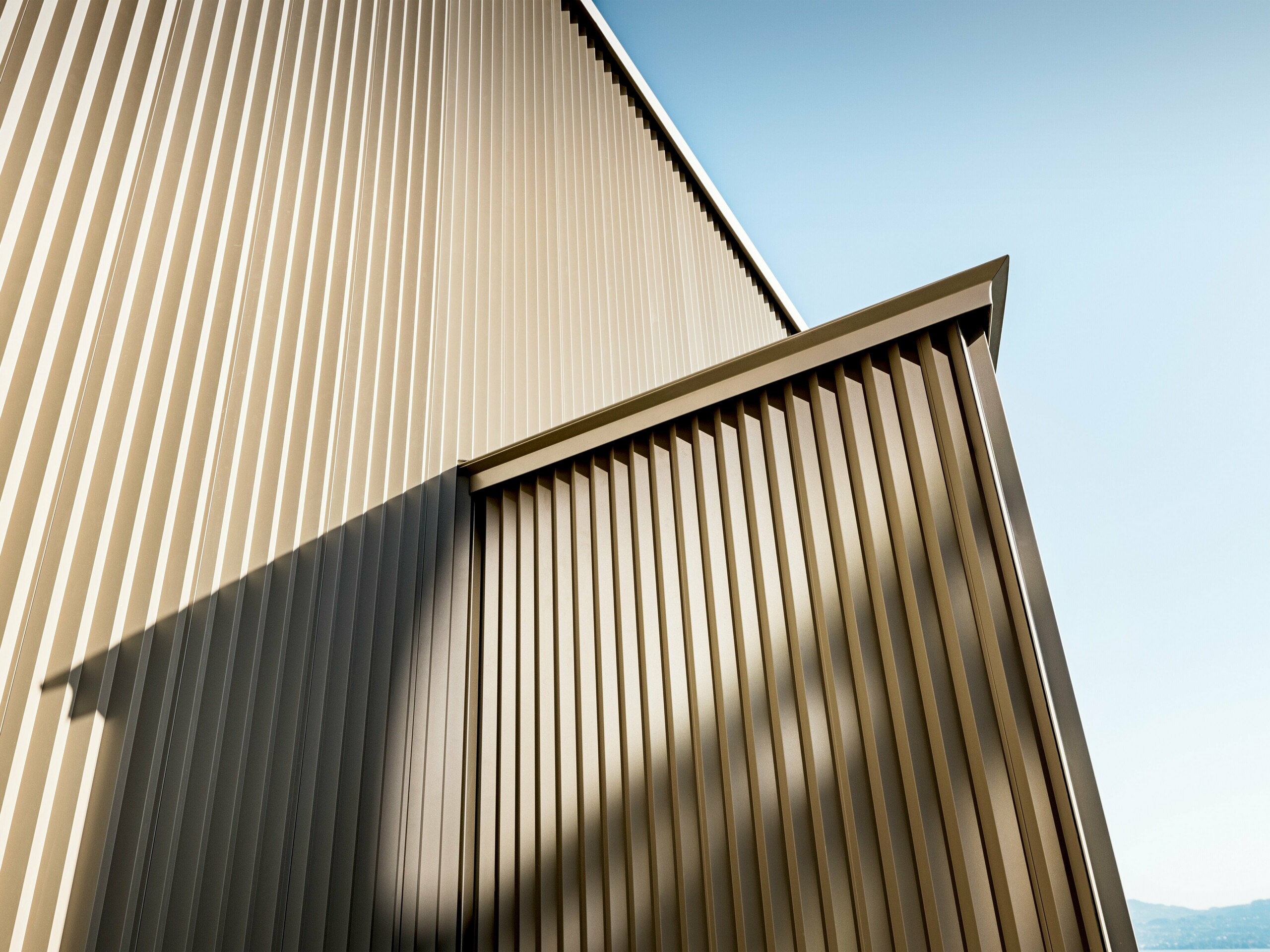 Elegante PREFA Aluminiumfassade in Bronzeoptik an einem Wohnhaus in St. Gingolph, entworfen von Architektin Sophie Morard. Die vertikal gezackten Individualprofile erzeugen ein faszinierendes Spiel aus Licht, Schatten und Struktur, das der Fassade Tiefe und Dynamik verleiht. Die hochwertige, pulverbeschichtete Oberfläche sorgt für langlebigen Schutz und stilvolle Ästhetik – ideal für anspruchsvolle Wohnbauprojekte. Die bronze schimmernde Gestaltung fügt sich harmonisch in die alpine Umgebung ein und macht das kleine Haus zu einem architektonischen Highlight mit großer Wirkung.