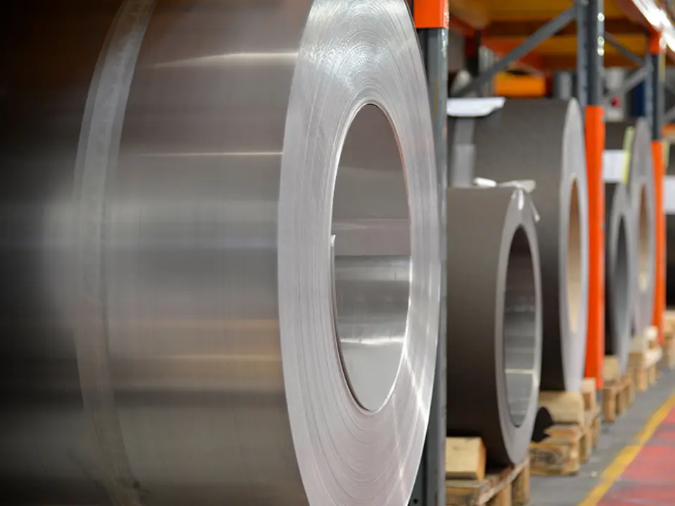 Aluminium rollen (coils) op houten palletten, op de voorgrond staat een aluminium rol in blank naturel, en daarachter zijn nog meer banden en platen van aluminium te zien.