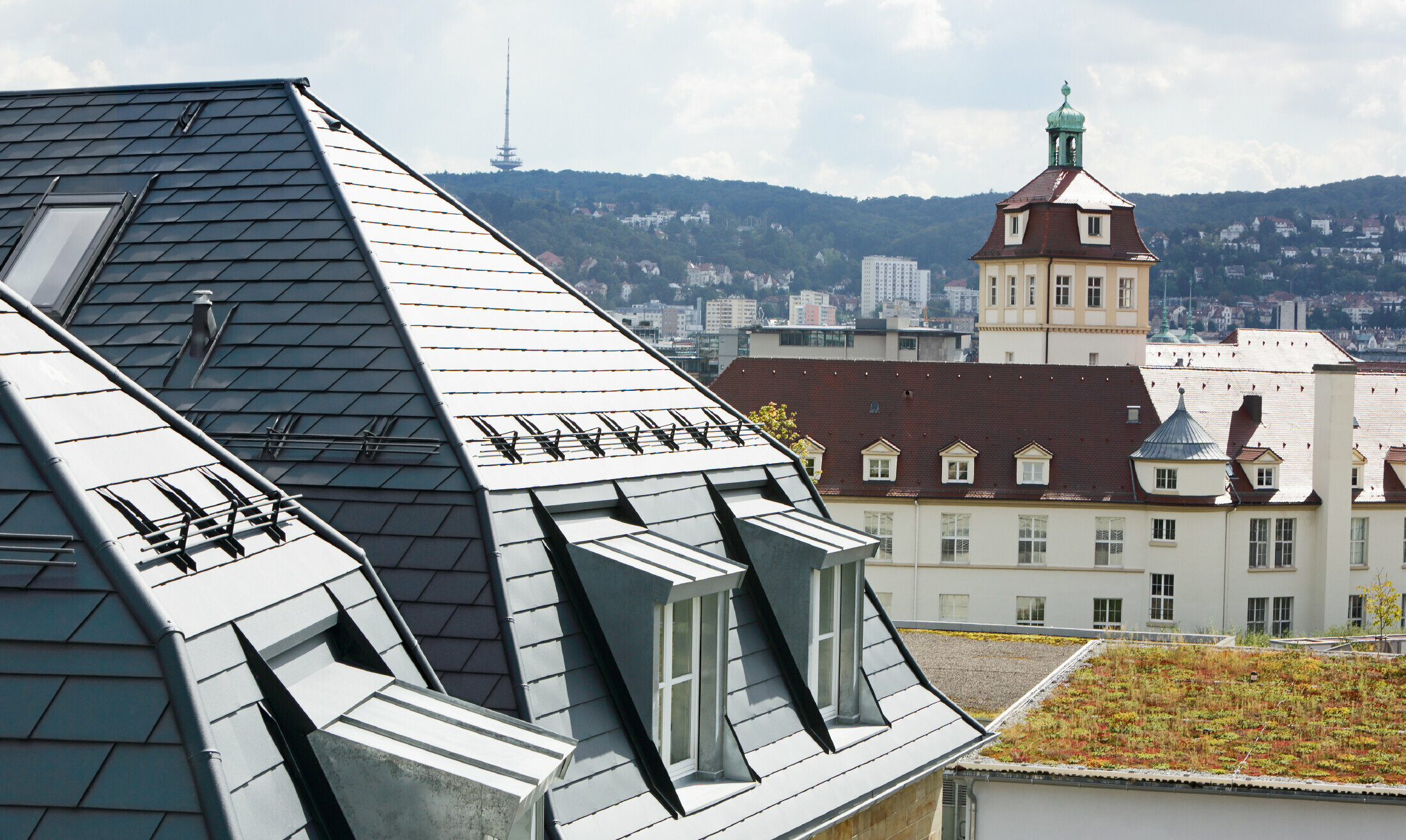 Oud stadshuis in Stuttgart met geknikt dak en veel dakkapellen, bedekt met de aluminium schindels van PREFA in P.10 antraciet