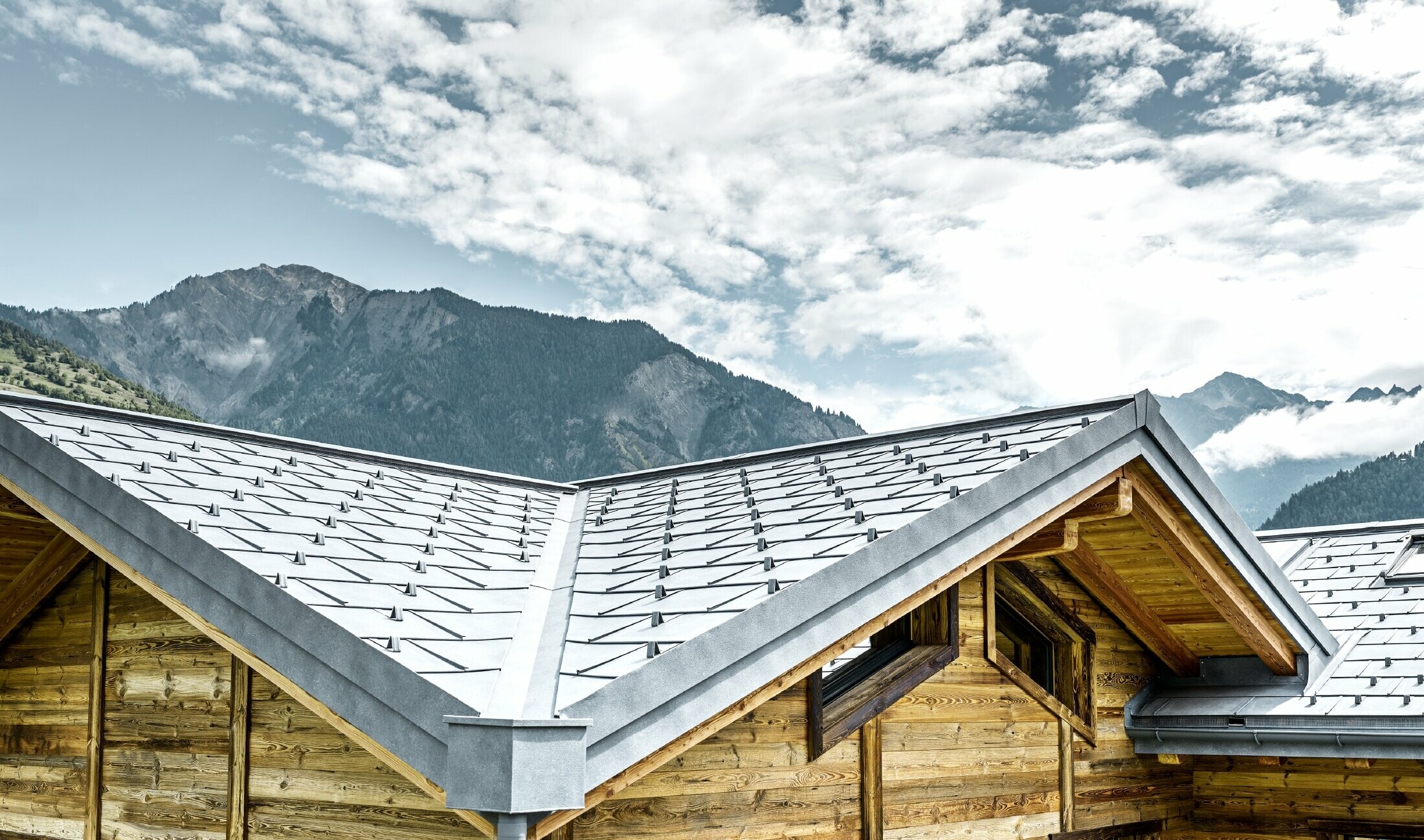 Dank van een rustieke alpenhut in Zwitserland met houten gevel en een aluminium dak van PREFA. Hiervoor is de dakpan R.16 in steengrijs gebruikt. Te herkennen zijn het hoekige dak en de kiel.
