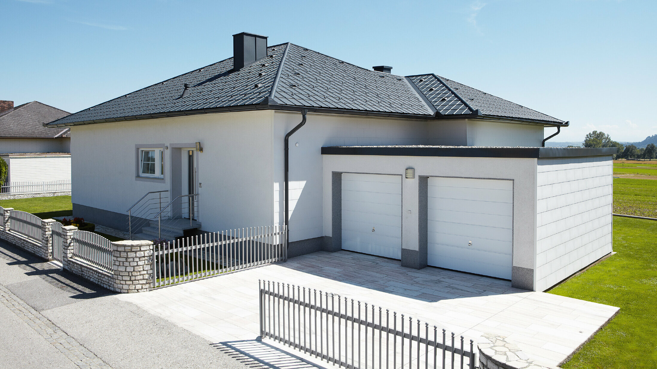 De nieuw gebouwde bungalow met tentdak werd bedekt met PREFA-dakpan in P.10 antraciet. Rechts werd een dubbele garage toegevoegd, gefotografeerd vanaf de straat.