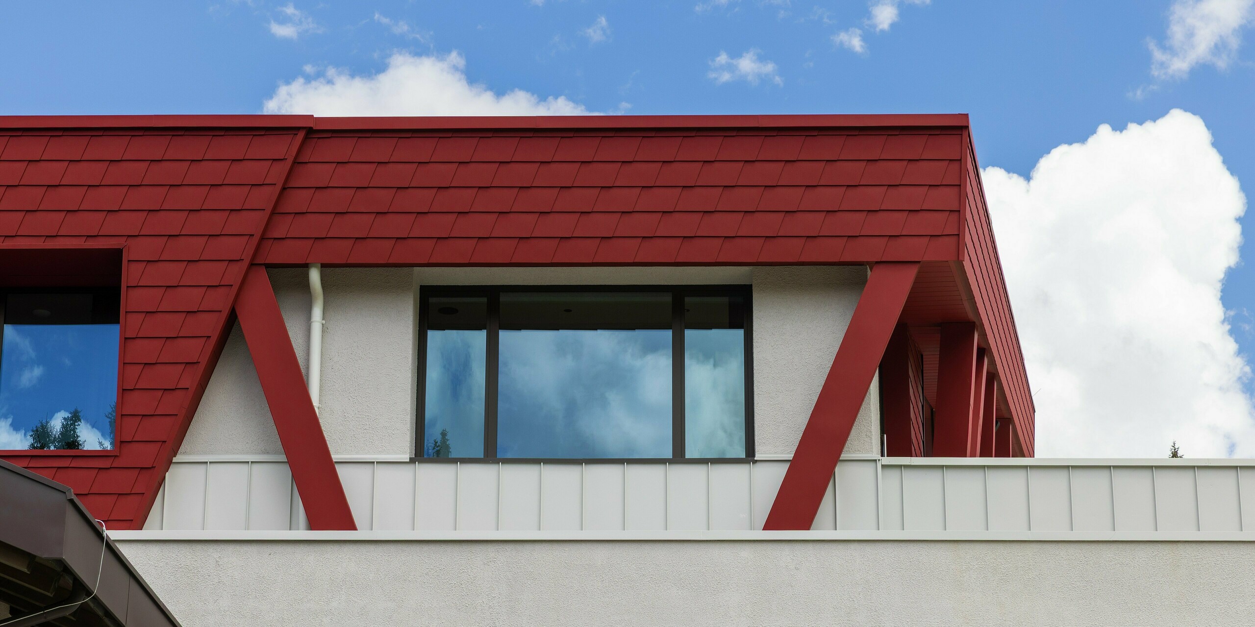 Die markante Gebäudehülle des Summit Mountain Clubs in Ratschings präsentiert die Farbe P.10 Oxydrot an der Fassade. Im Vordergrund der Perspektive stehen die präzise verlegten PREFA Wandschindeln und ein auffälliger roter Stützträger. Diese robusten Materialien bieten optimalen Schutz gegen das raue Bergklima und verleihen dem Restaurant ein modernes, auffälliges Design.