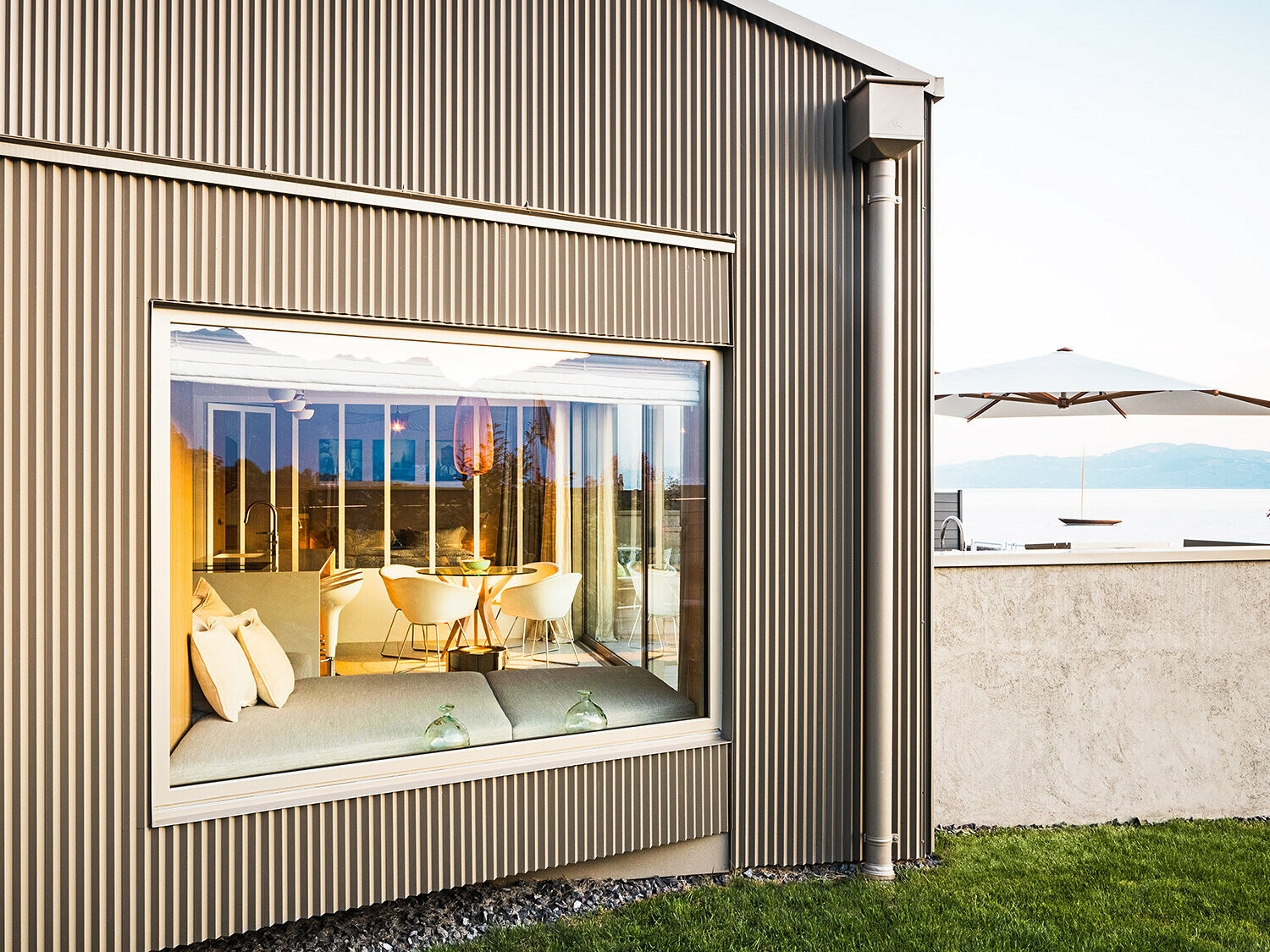 Zijaanzicht van het gebouw met aluminiumgevel en kartelprofiel, een deel van het verlichte interieur is te zien.